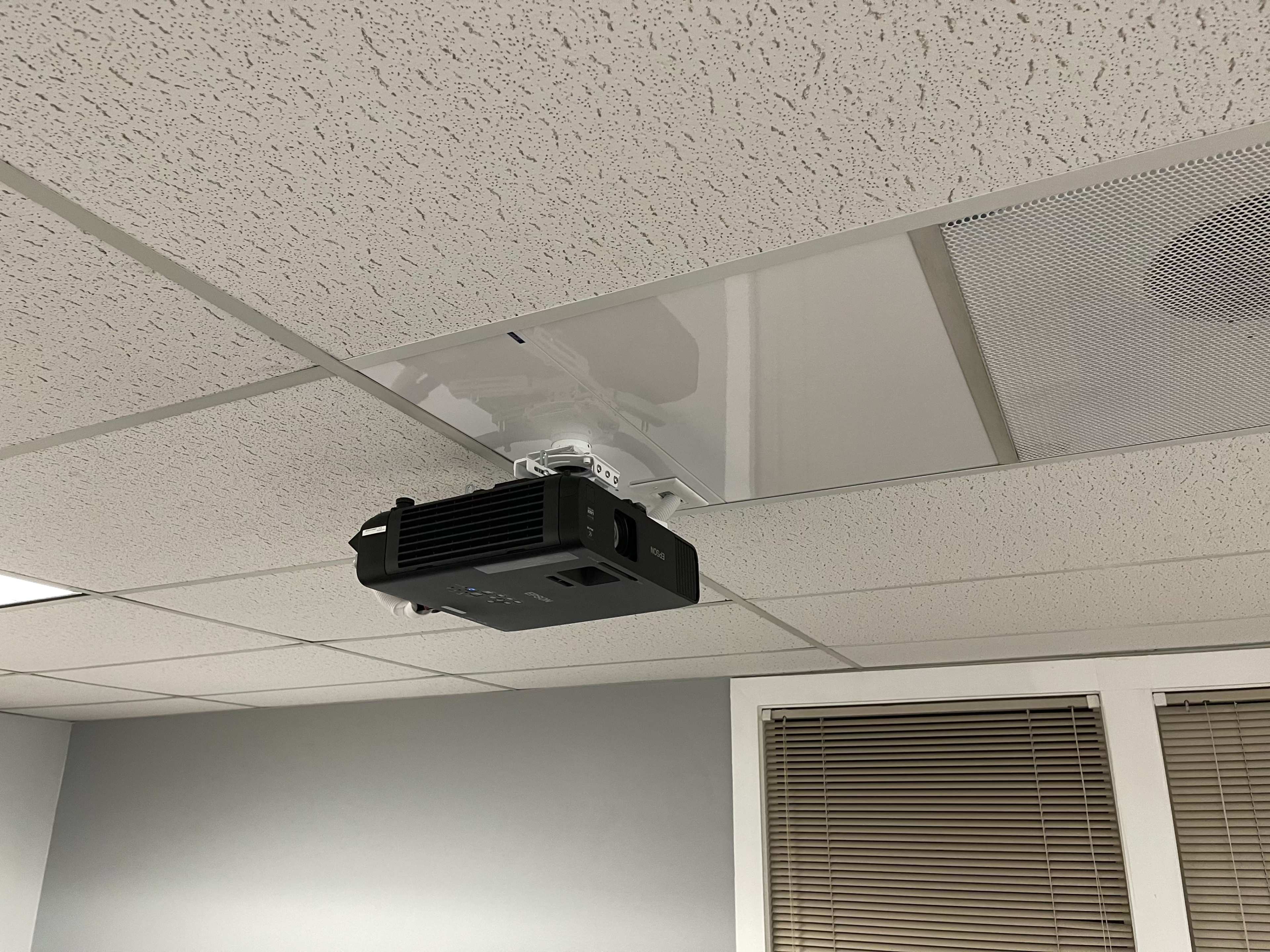 The image shows a ceiling-mounted projector installed in an office environment.
