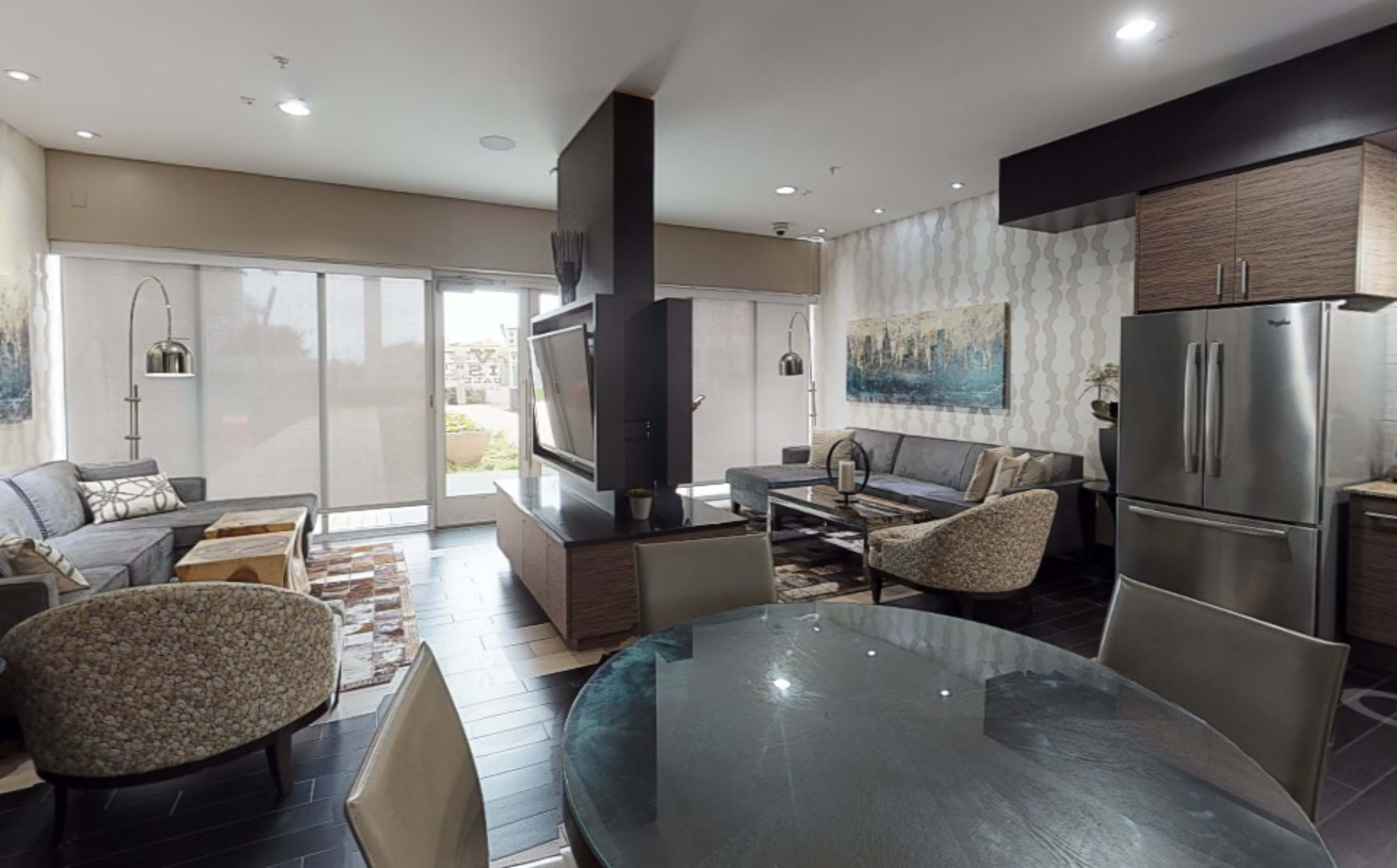 A modern living room and dining area with contemporary furniture, a large television, and large windows providing natural light.