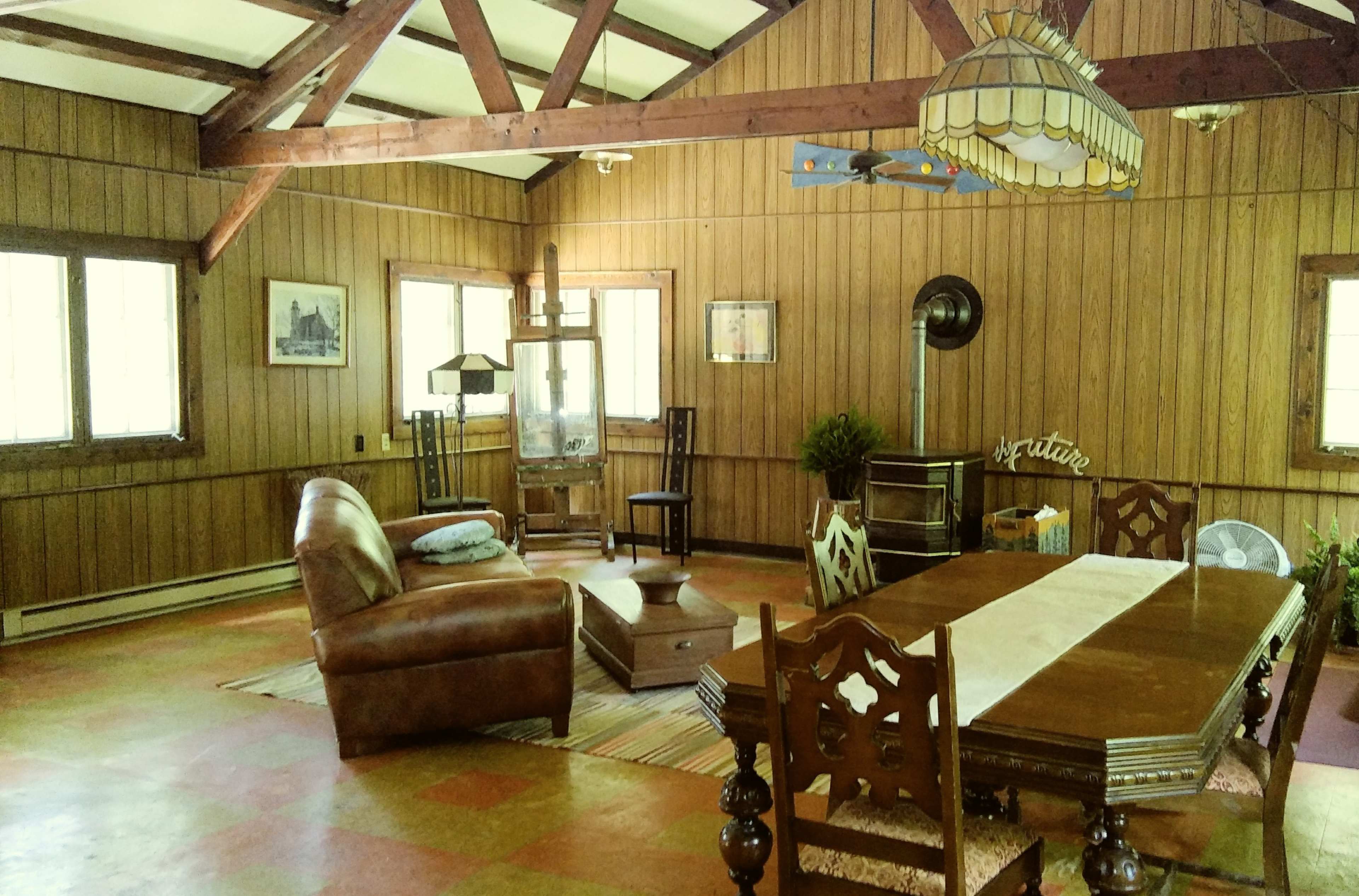 The interior of a rustic room features wooden paneling, a leather sofa, a dining table, and various furnishings arranged around a central area.