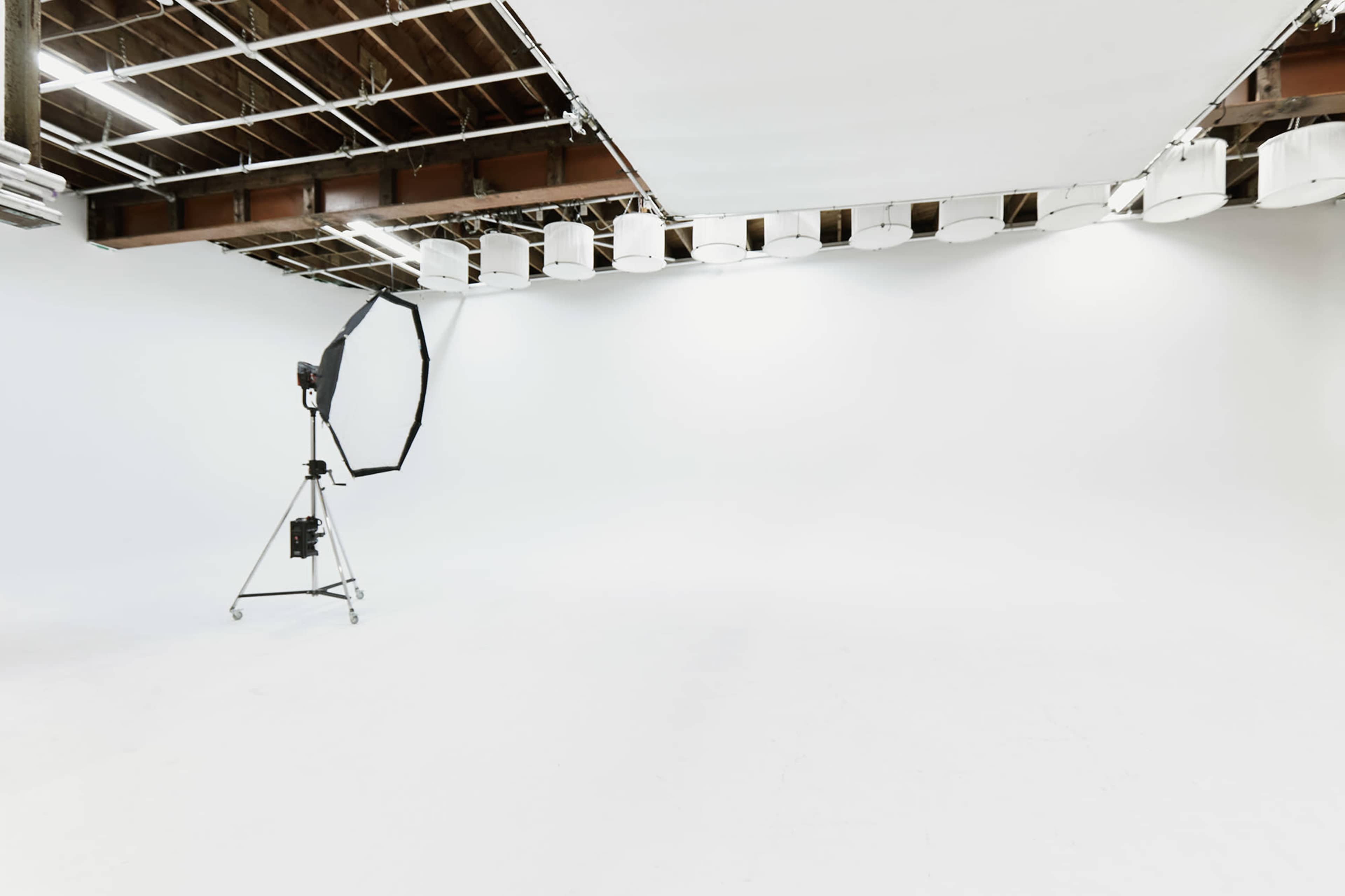 The image shows a spacious photography studio with white walls and a backdrop, featuring a large softbox light on a stand.