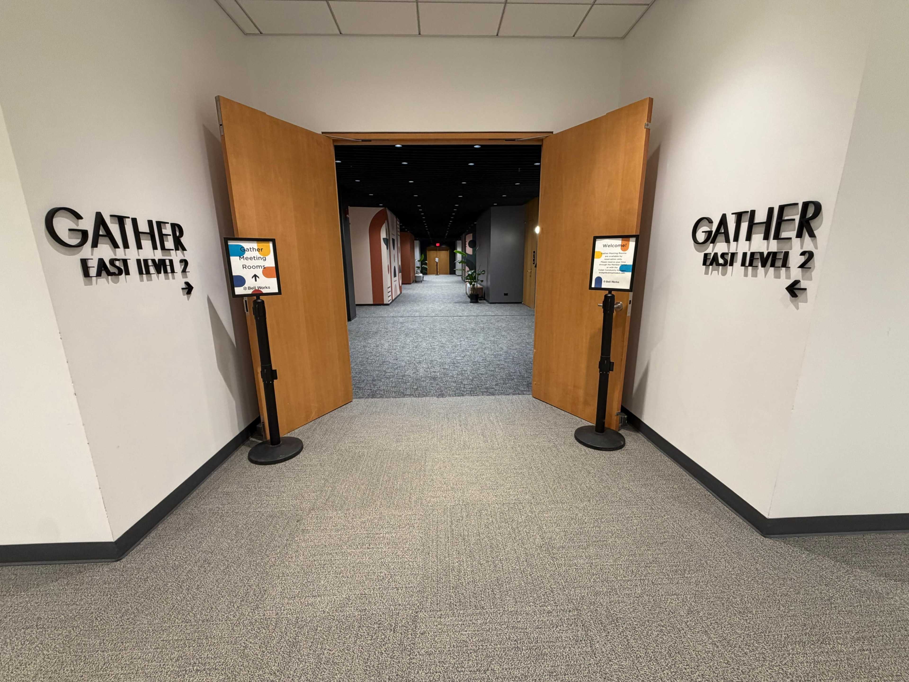 The image shows a wide hallway with open double doors leading to a sign labeled "GATHER EAST LEVEL 2" and directional signs on either side.