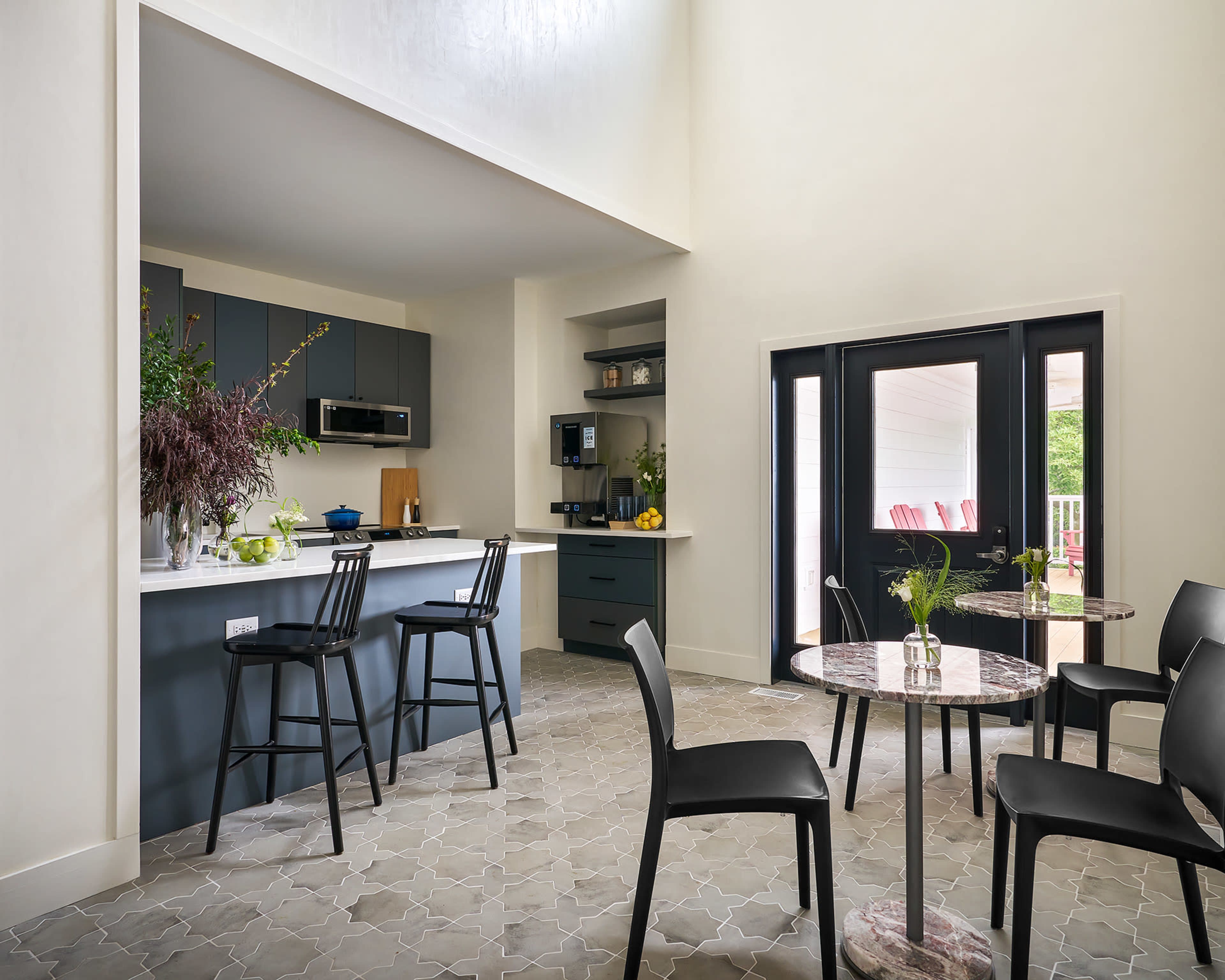 A modern kitchen features dark cabinetry and a dining area with black chairs around a marble-topped table.