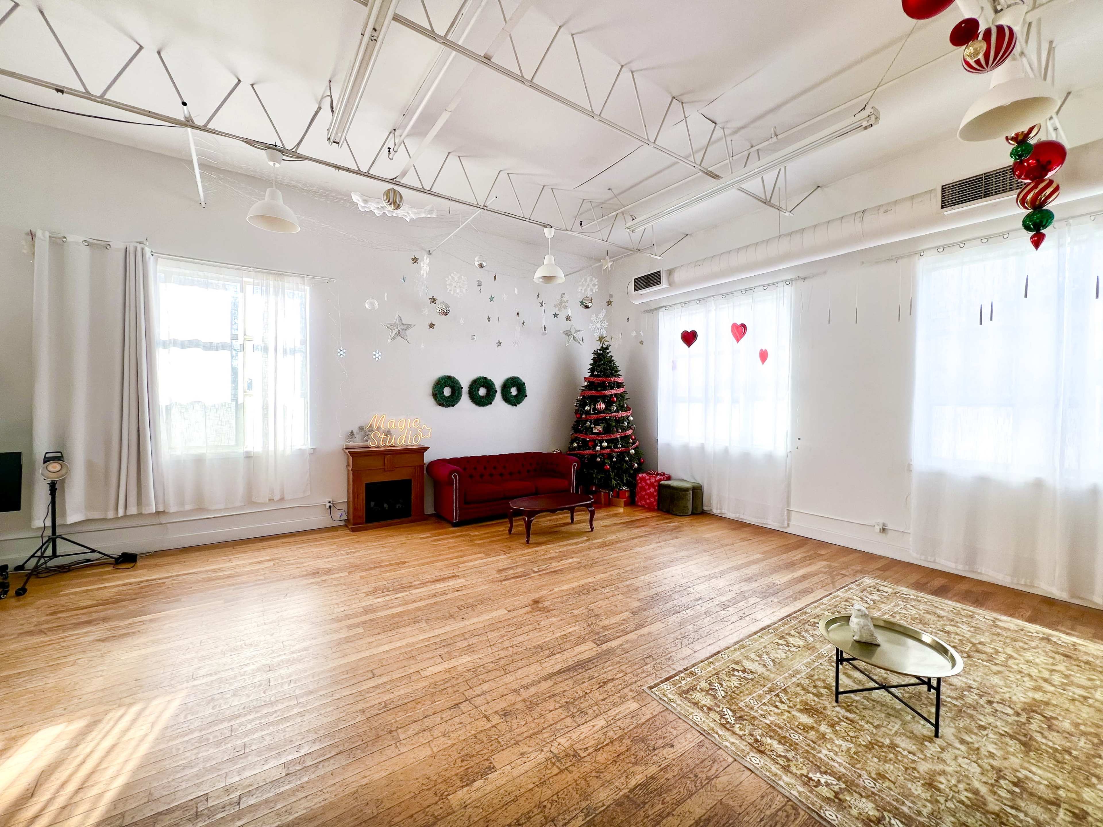 A spacious room features a red sofa, a Christmas tree decorated with ornaments, and heart-shaped decorations hanging from the ceiling.