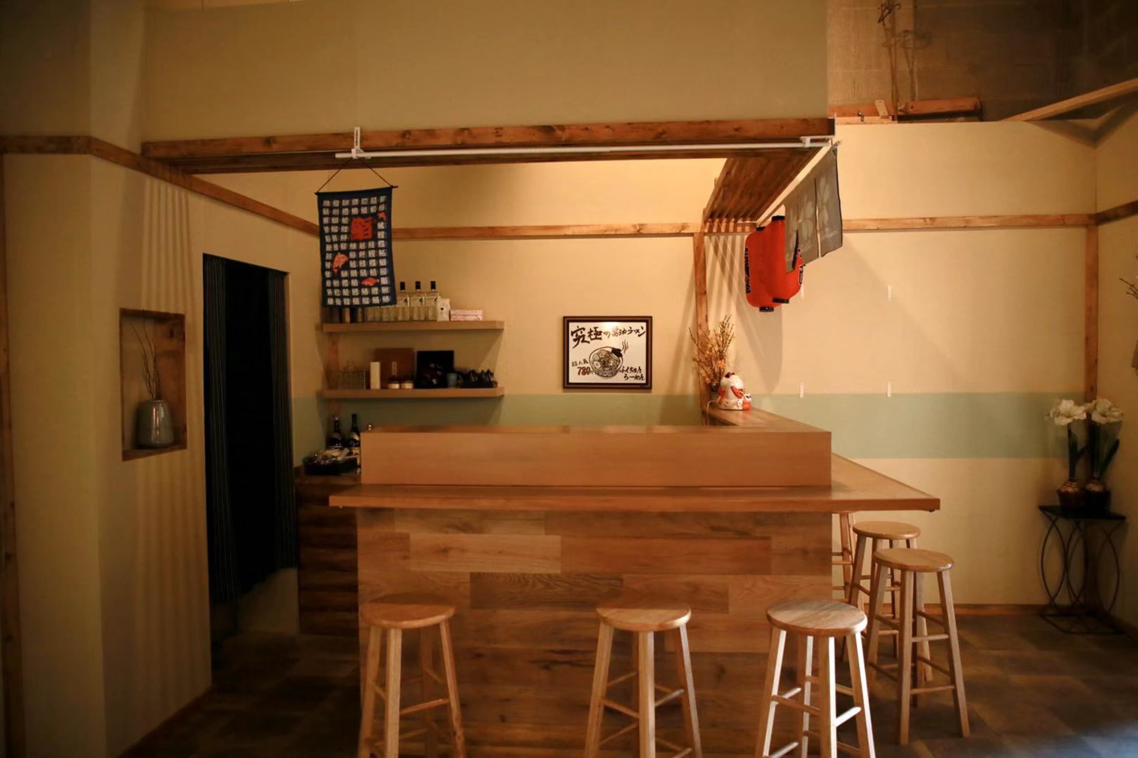 A wooden bar with four stools is set against a wall adorned with minimalist decor in a softly lit room.