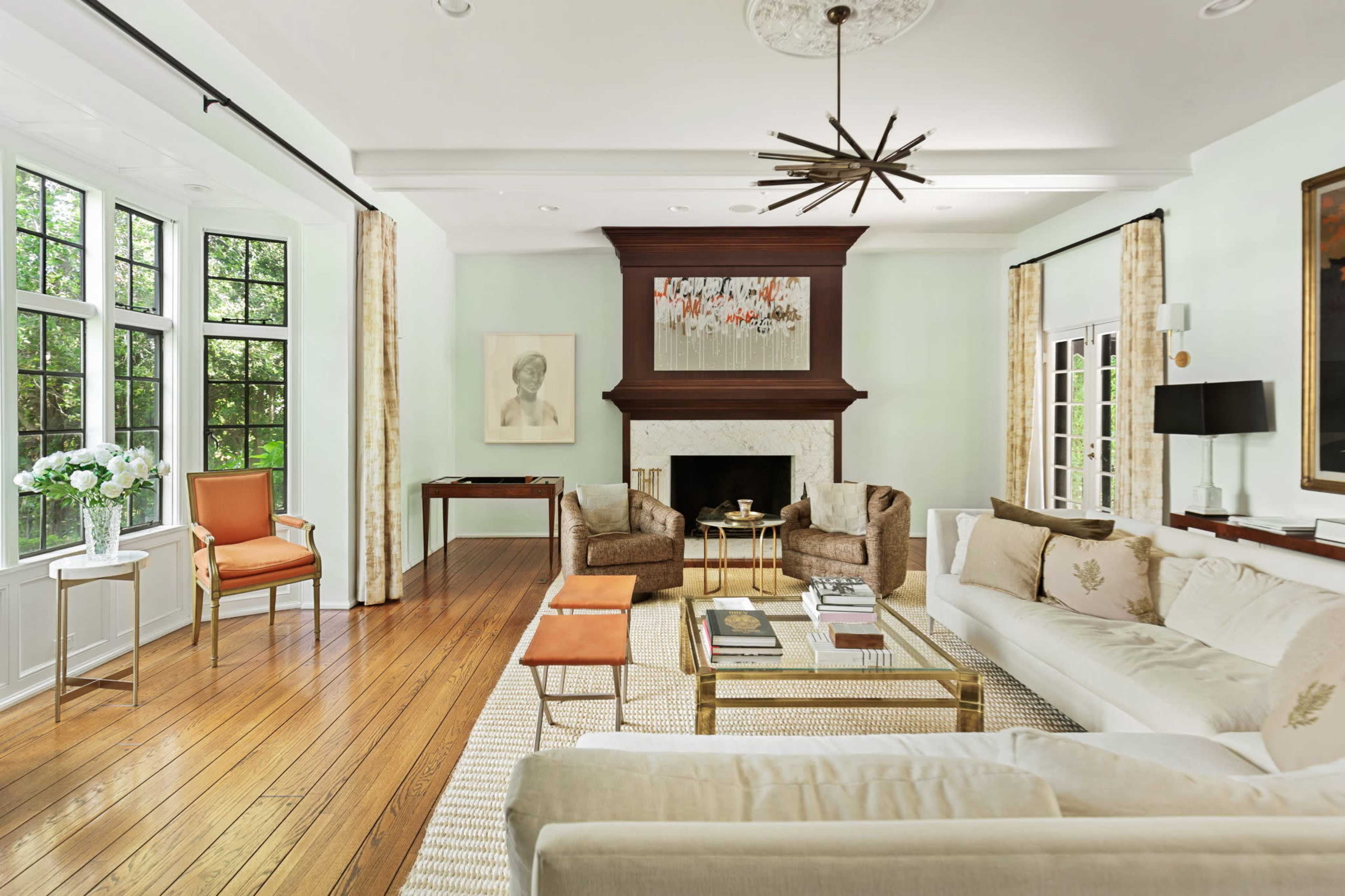 The living room features a light green color scheme, hardwood floors, large windows, and a central fireplace with surrounding seating areas.