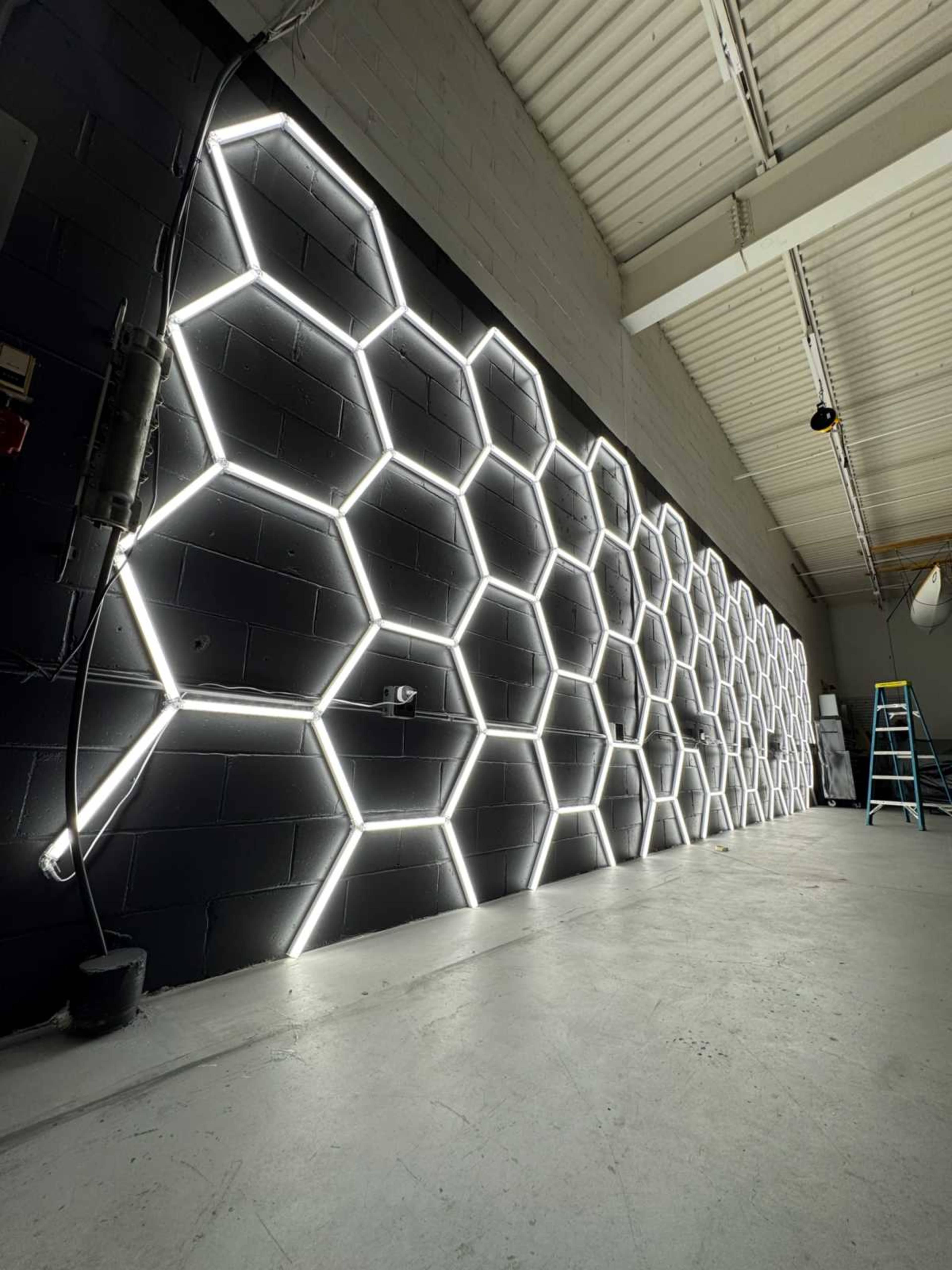 The image shows a wall decorated with a honeycomb pattern made of illuminated hexagonal light fixtures in a spacious, industrial-looking interior.