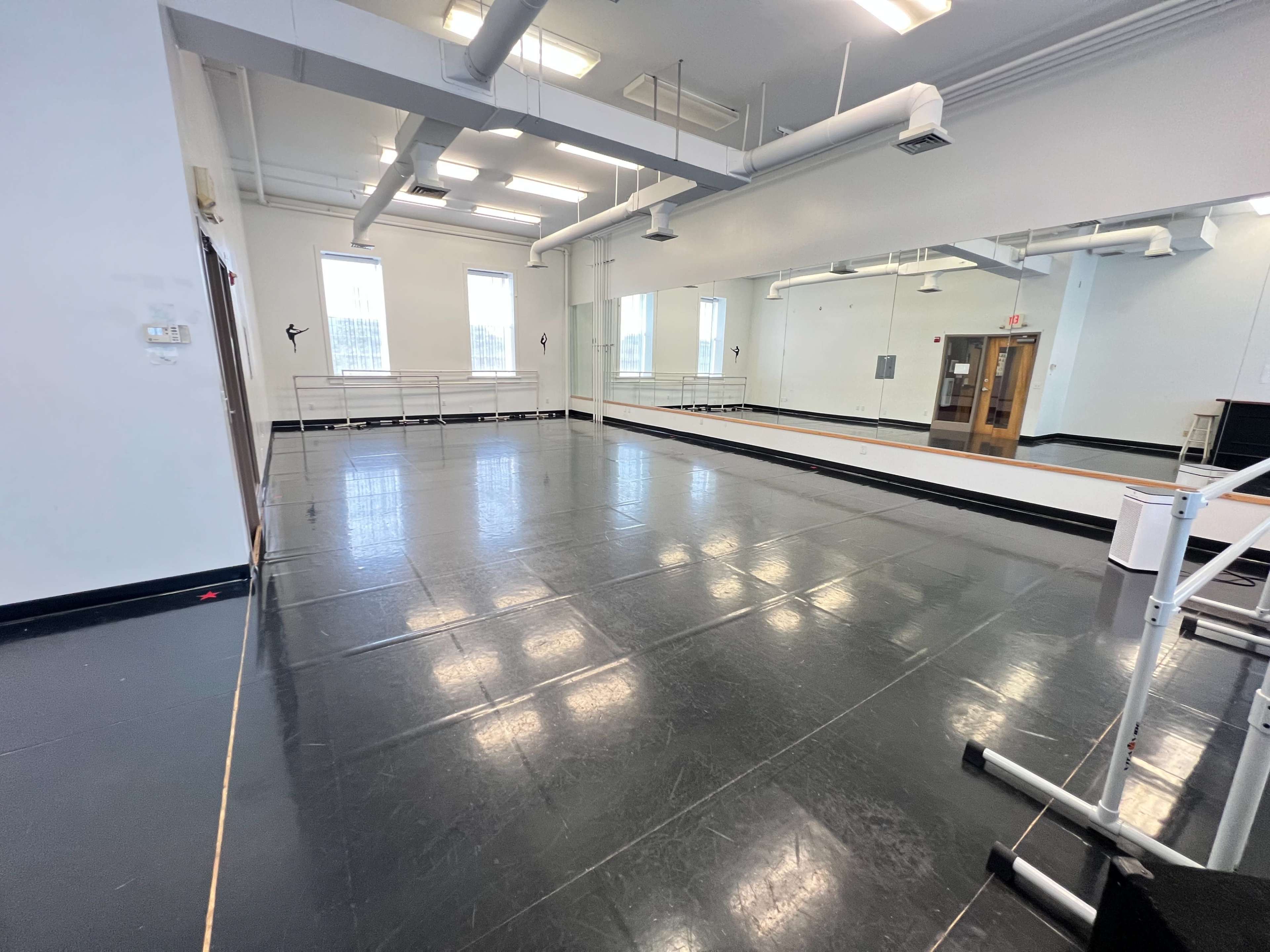 An empty dance studio with a mirrored wall and a polished black floor.