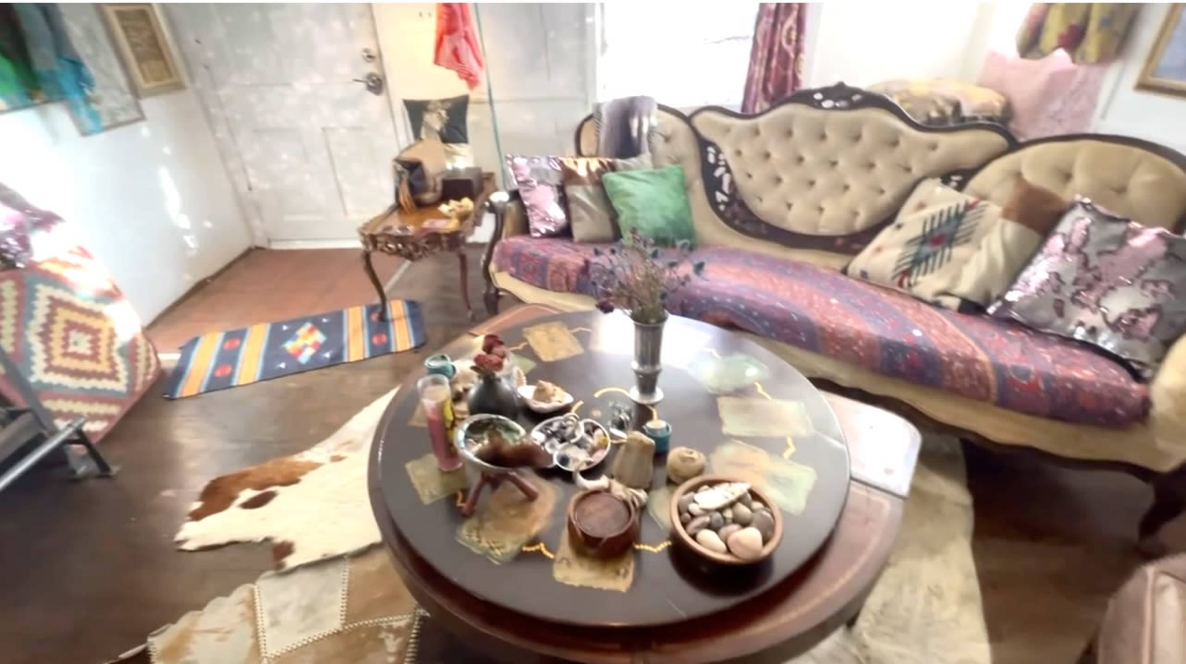 A cozy living room featuring a vintage sofa with colorful cushions, a round table adorned with decorative items, and a patterned rug on the floor.