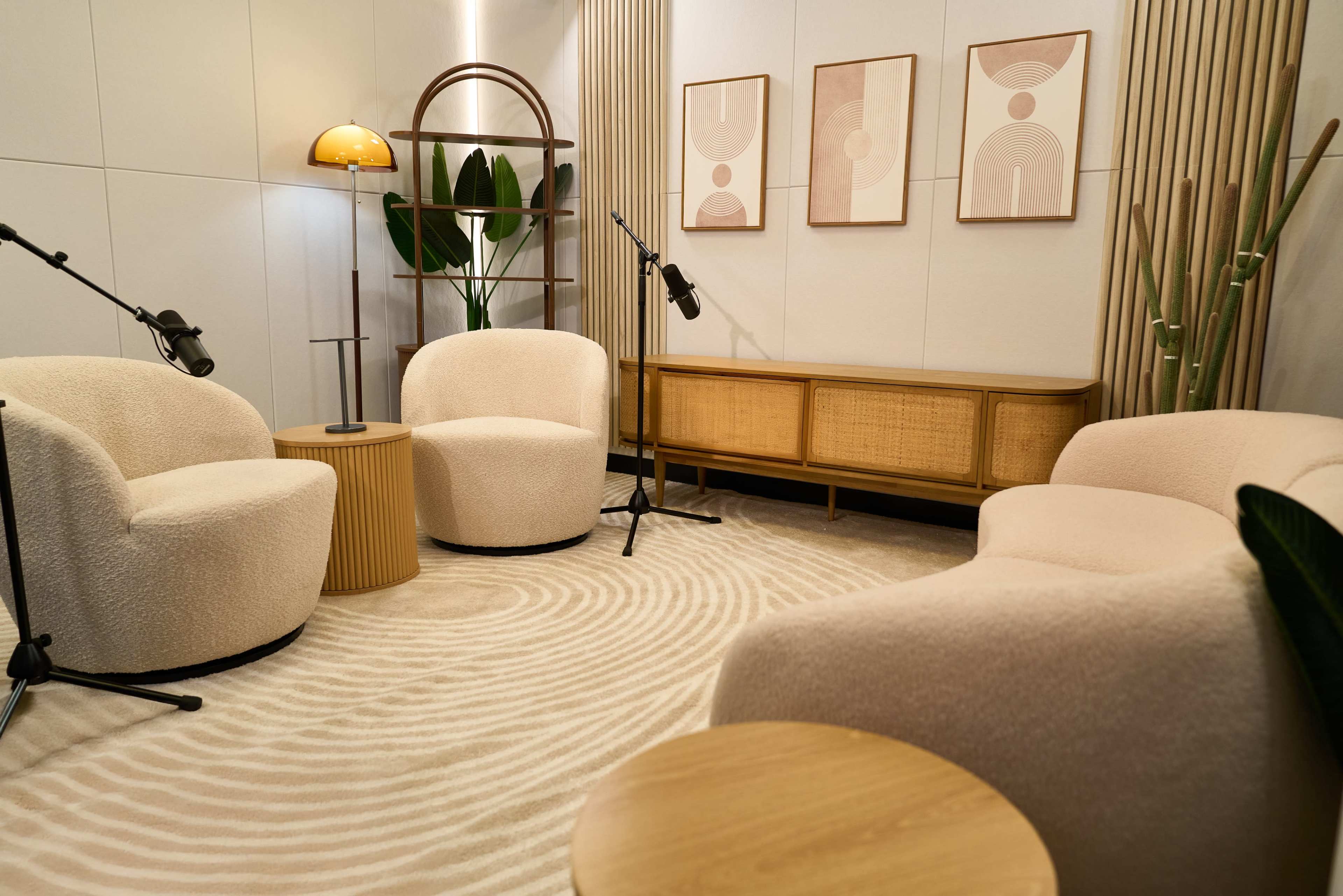 The image shows a modern, cozy interior setting with two plush armchairs, a circular table, and wall-mounted artworks, all arranged around a carpet with a wavy pattern.