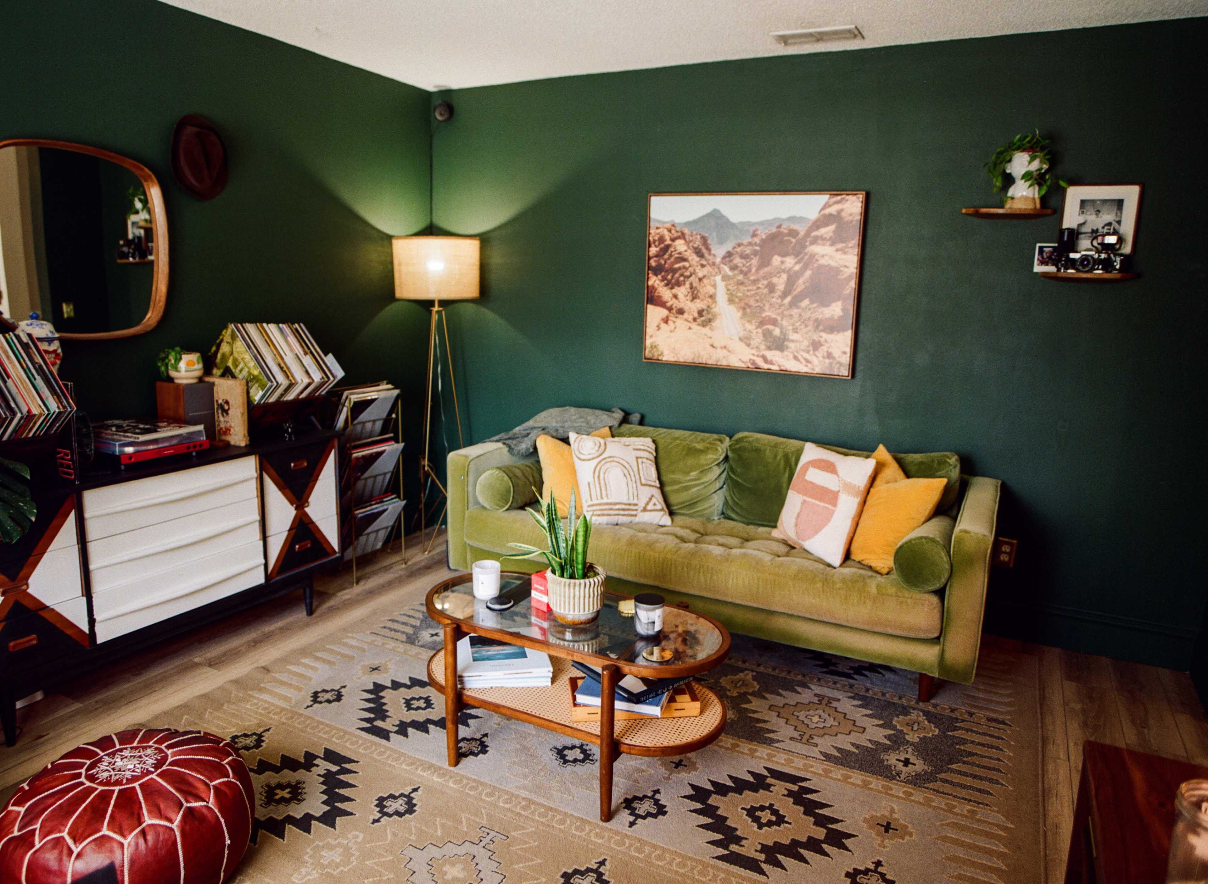 The image shows a cozy living room with a green accent wall, a plush green sofa, a round coffee table, and decorative items on shelves.