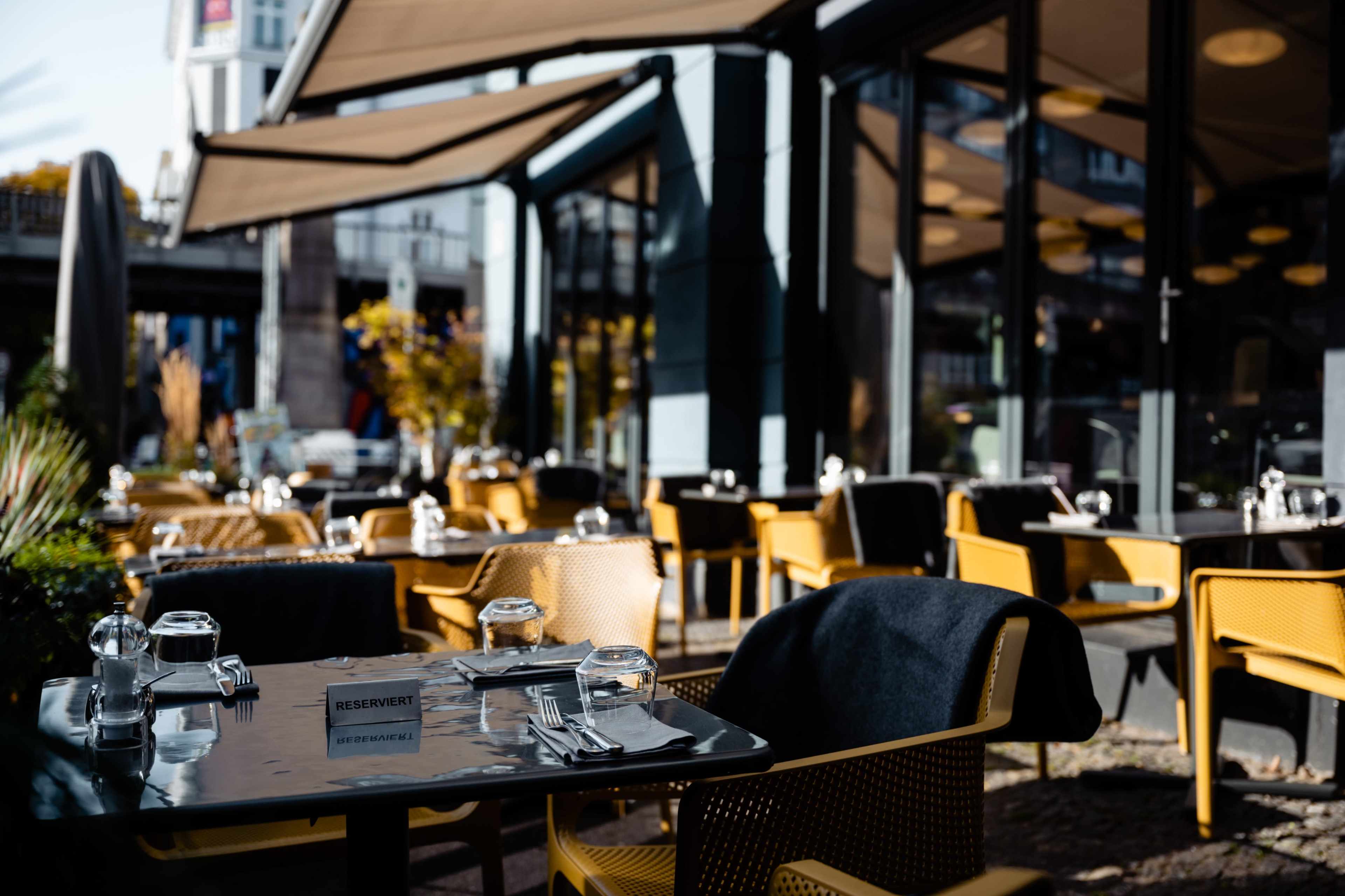 A restaurant patio features neatly set tables with reserved signs, surrounded by golden autumn foliage.