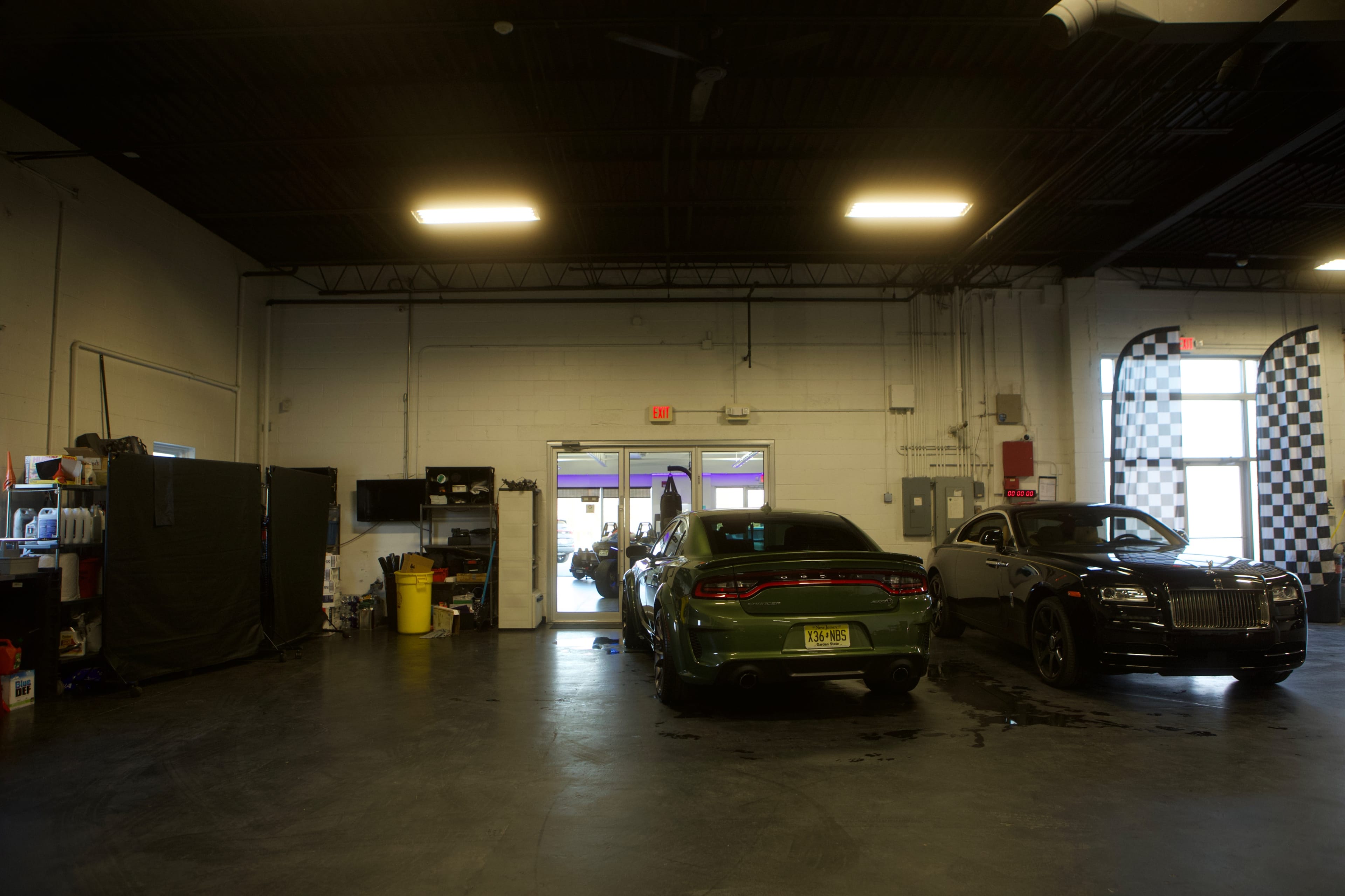 A garage space with two cars parked inside, one green and one black, and a doorway leading to another area.