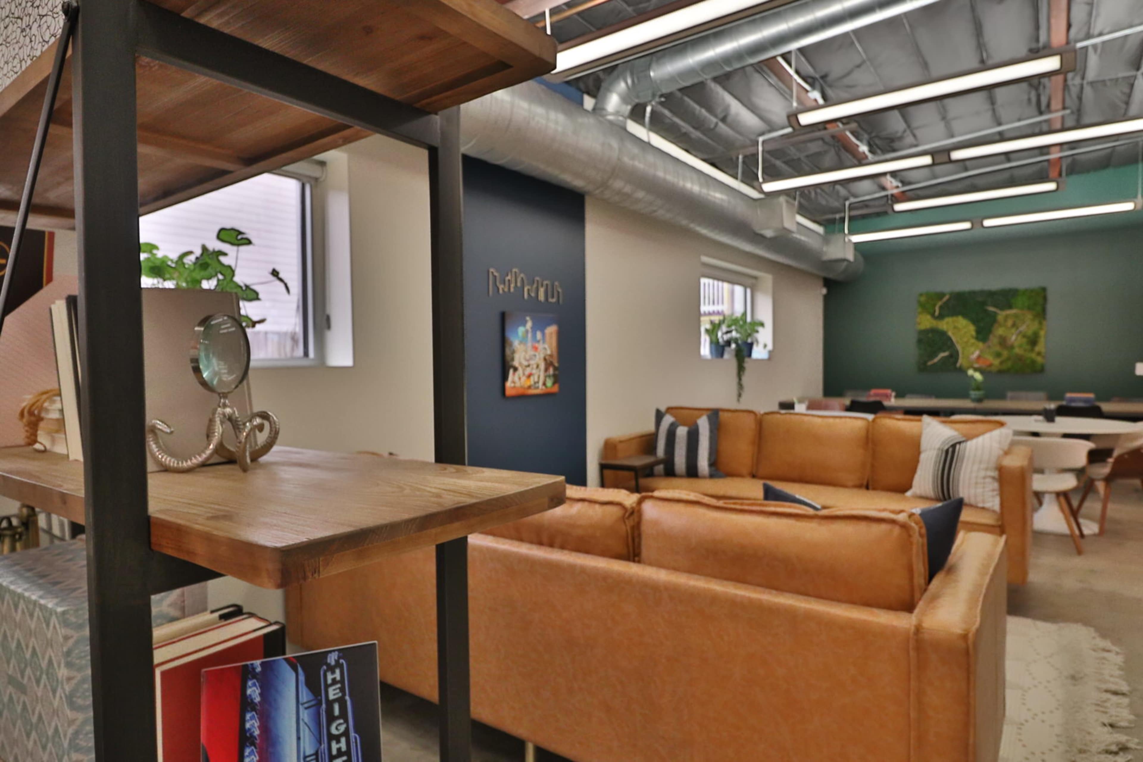 The image shows a modern interior space with brown leather sofas, a bookshelf, and a green accent wall featuring a piece of artwork.