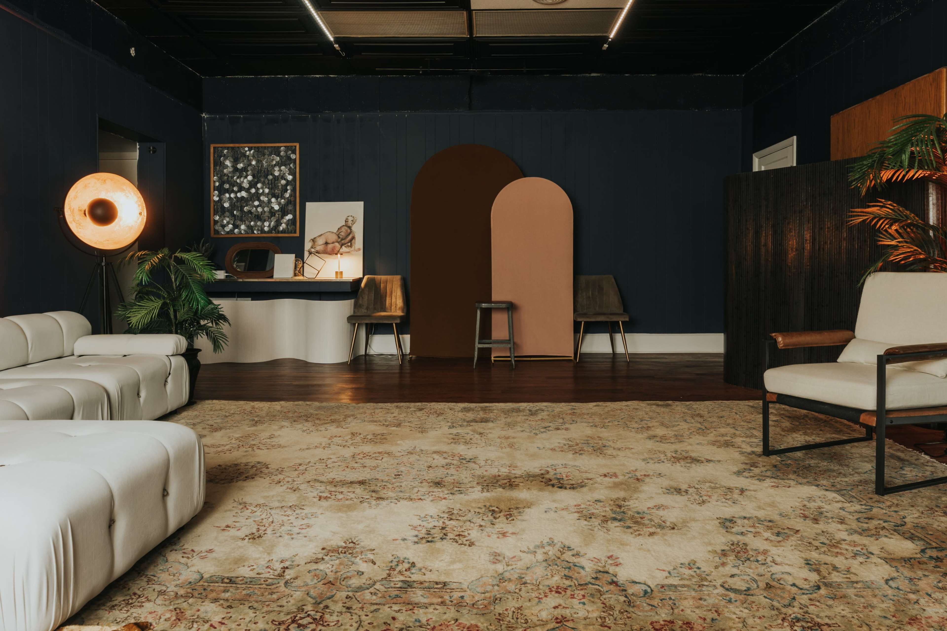 A modern, styled interior space featuring a seating area with white sofas, a large area rug, and various decorative elements including a floor lamp and wall art.