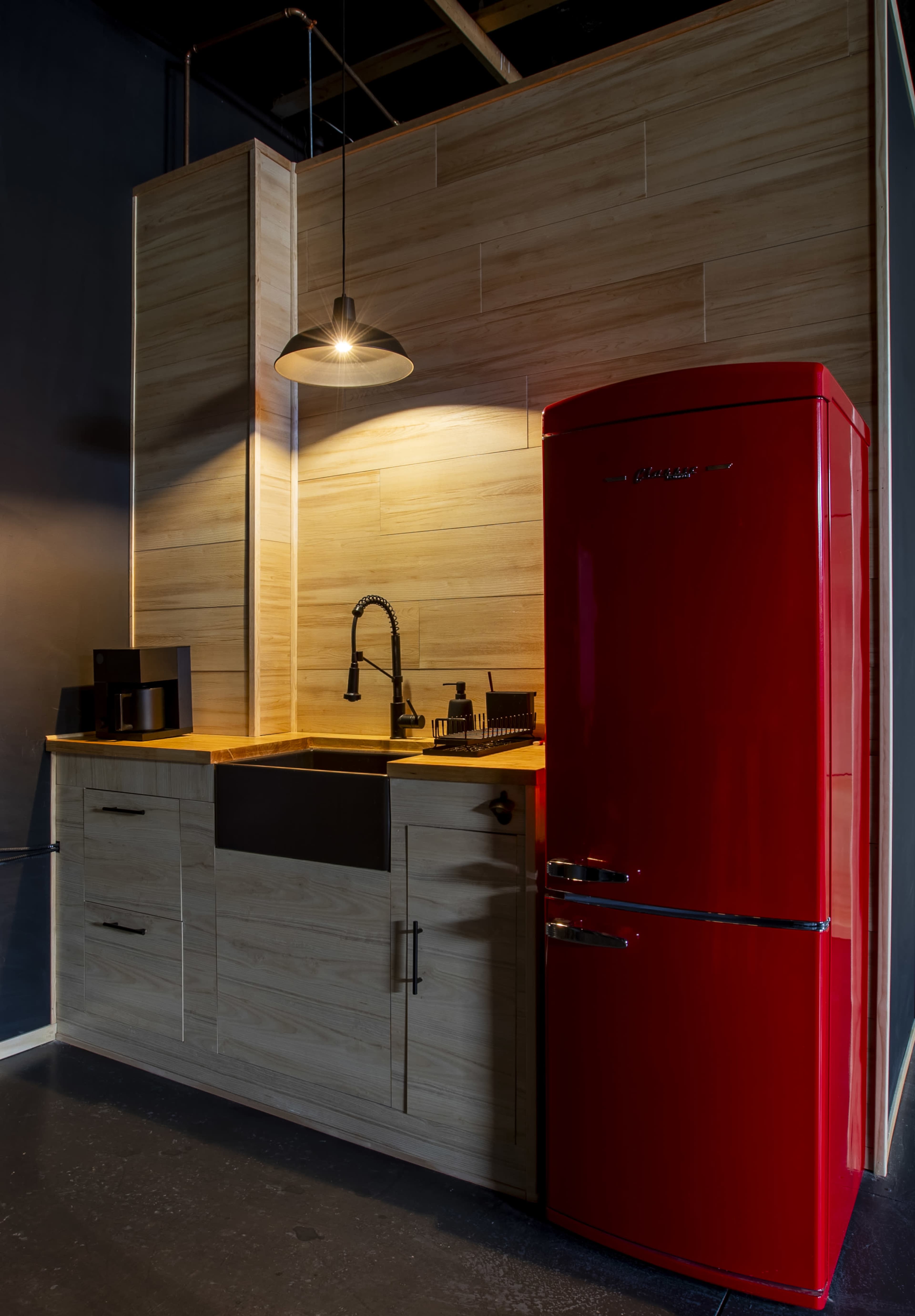 The image shows a modern kitchen setup featuring a red refrigerator, a black sink, and wooden cabinetry against a dark wall.