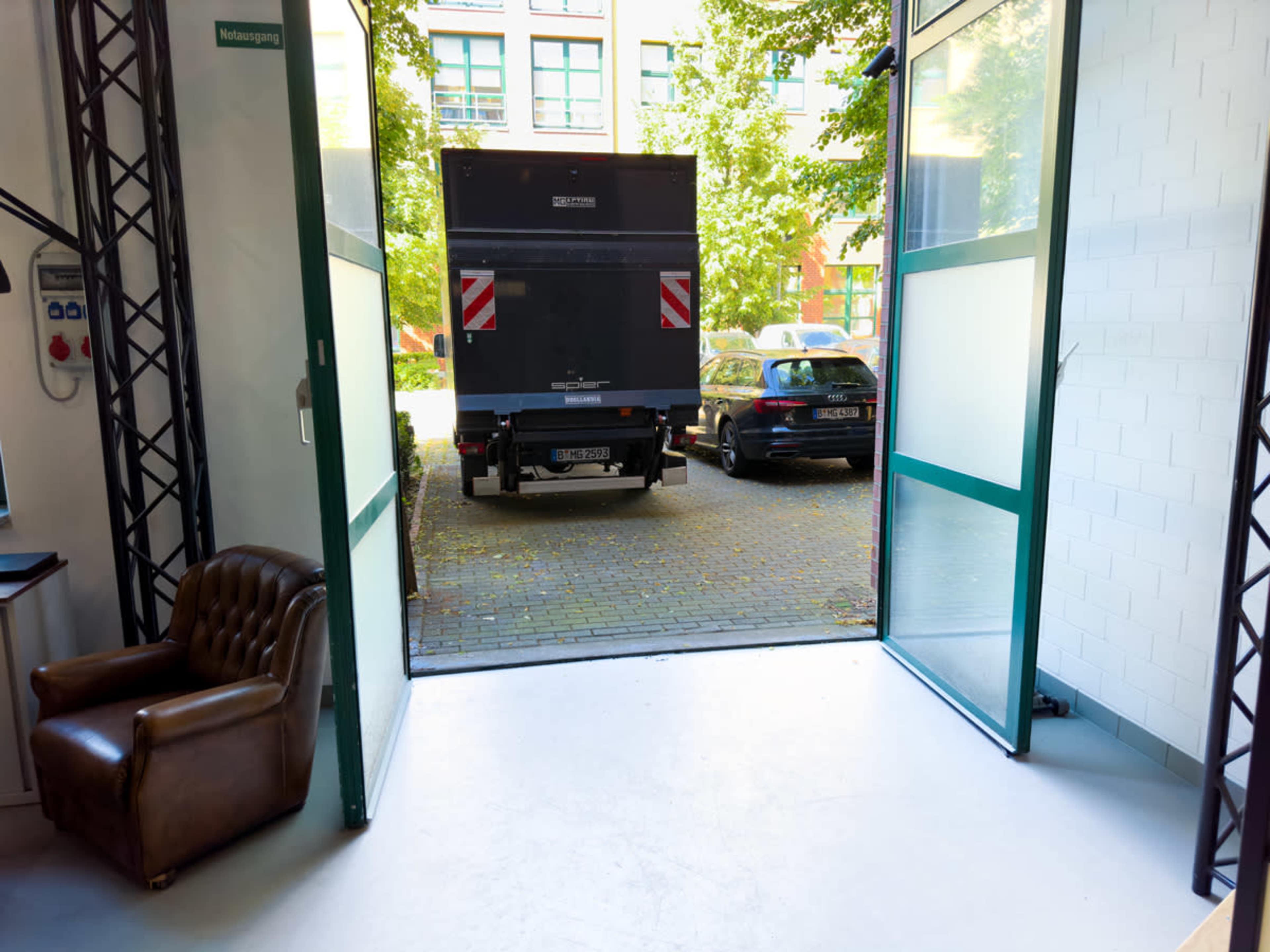 A truck is parked in a courtyard visible through open glass doors.