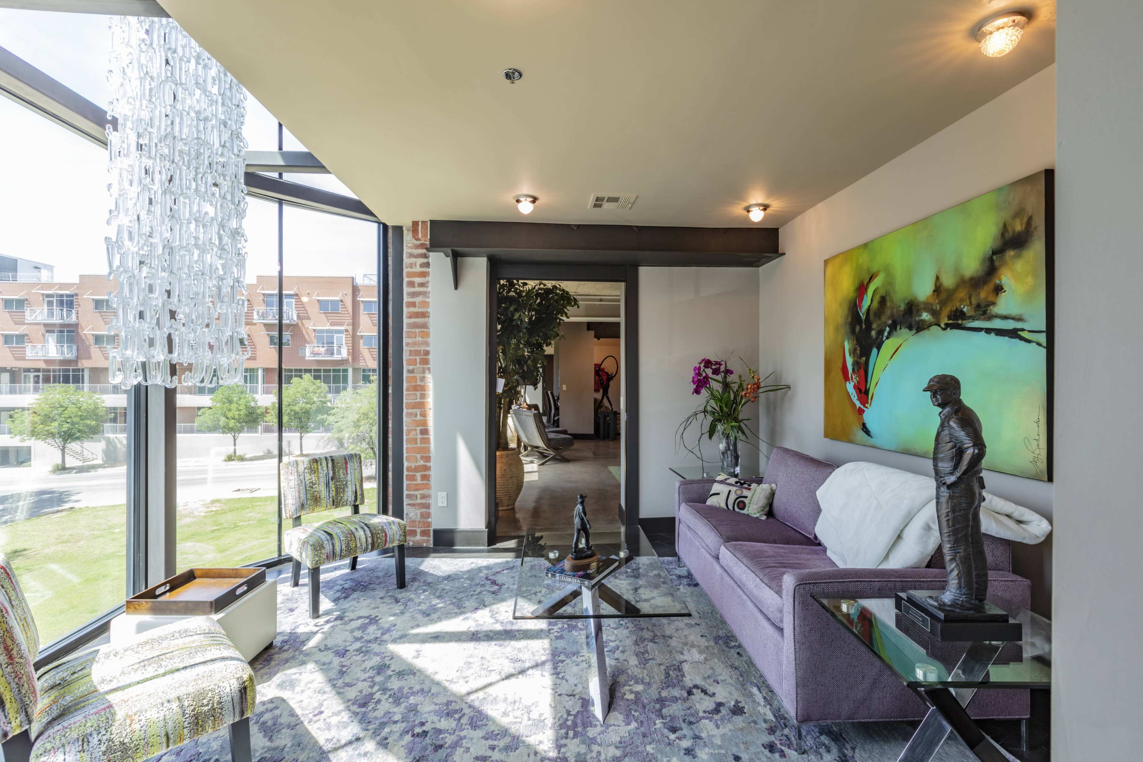 A modern living room with a purple sofa, glass coffee table, and a large window overlooking an outdoor space.