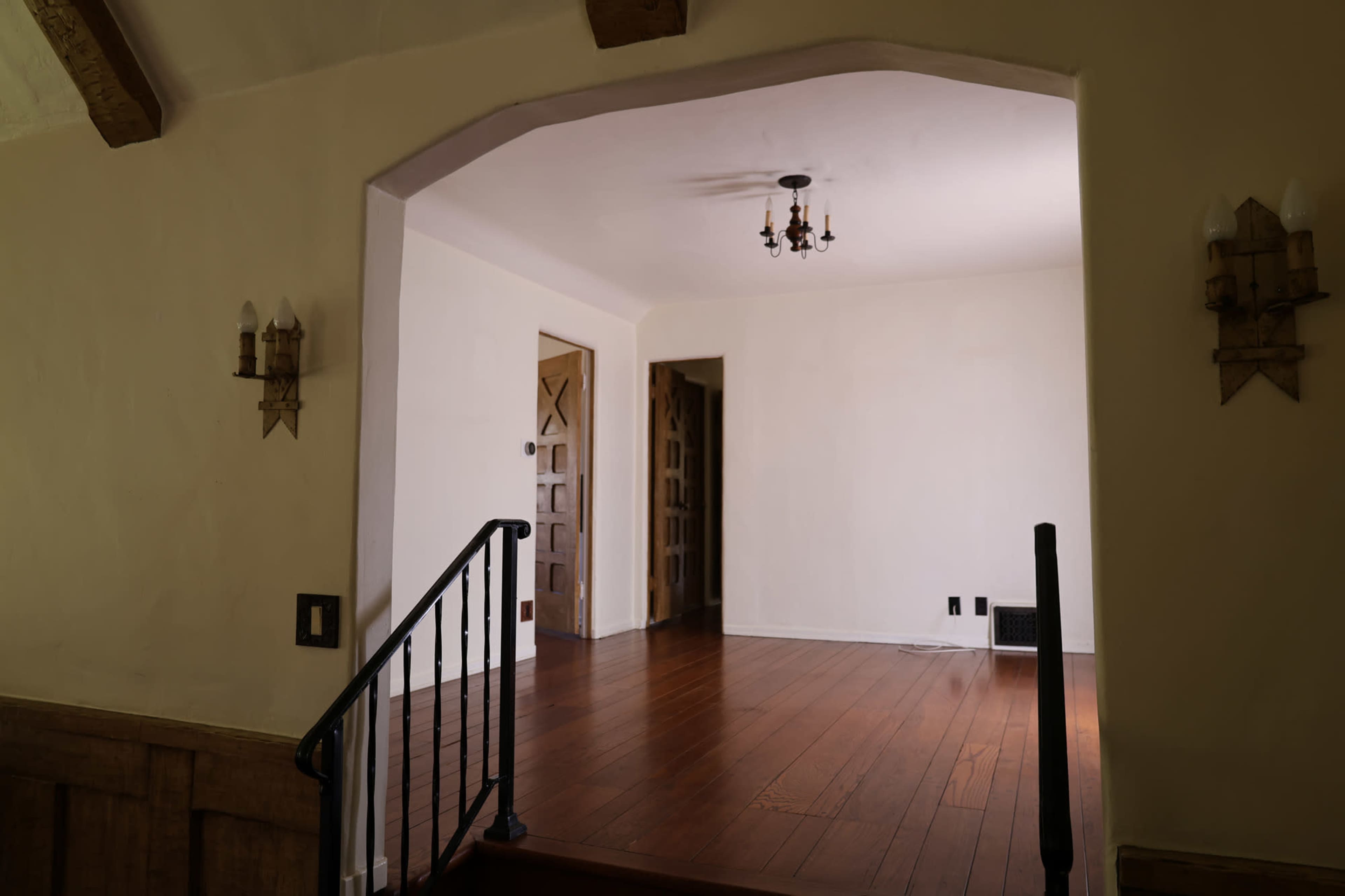 The image shows a well-lit interior space featuring a wooden floor, two doorways, and wall-mounted sconces.