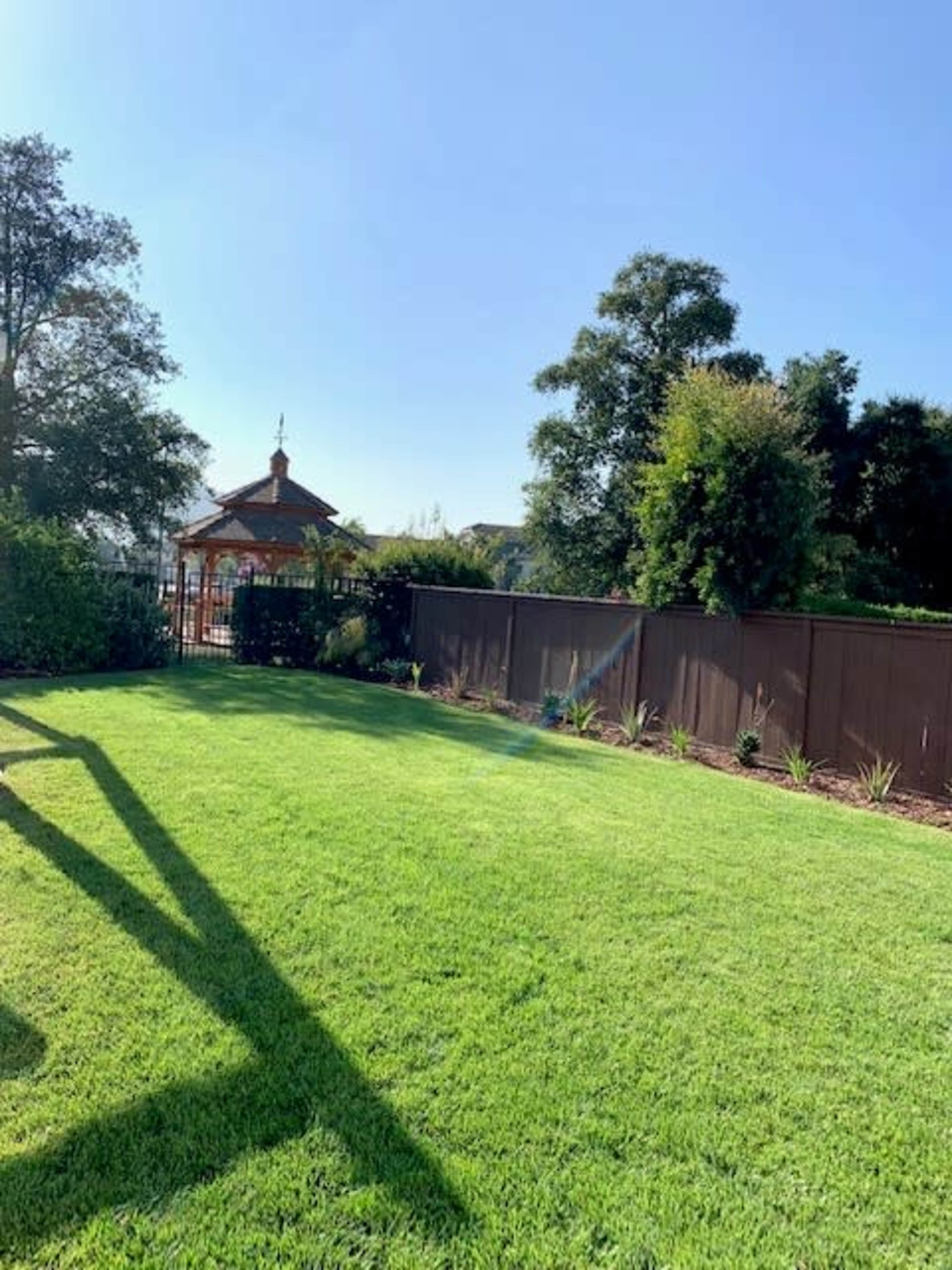 A well-maintained grassy lawn with a gazebo in the background and a fence lined with plants.