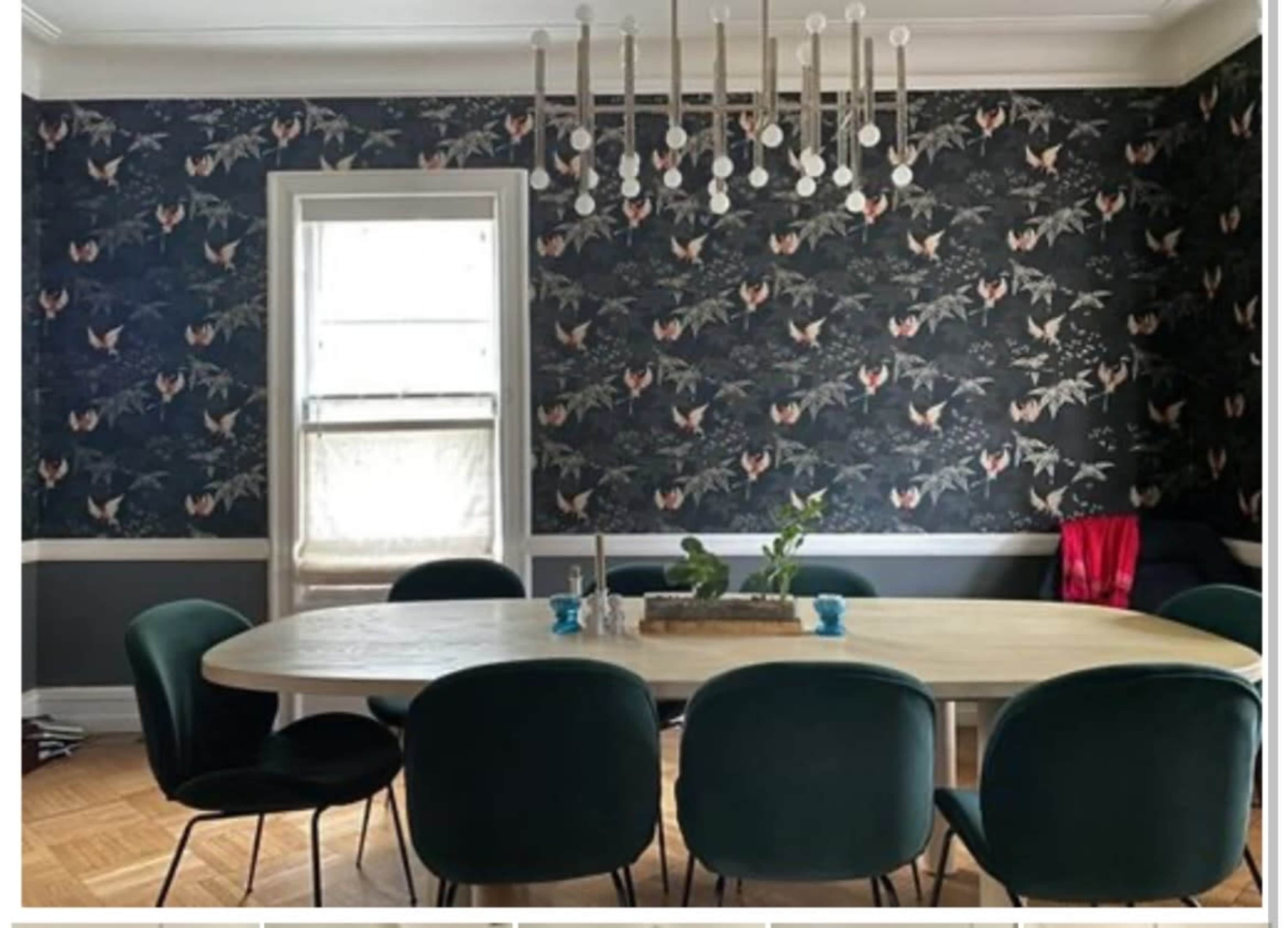 The image shows a modern dining room featuring a circular wooden table surrounded by green chairs, with patterned wallpaper and a decorative chandelier above.