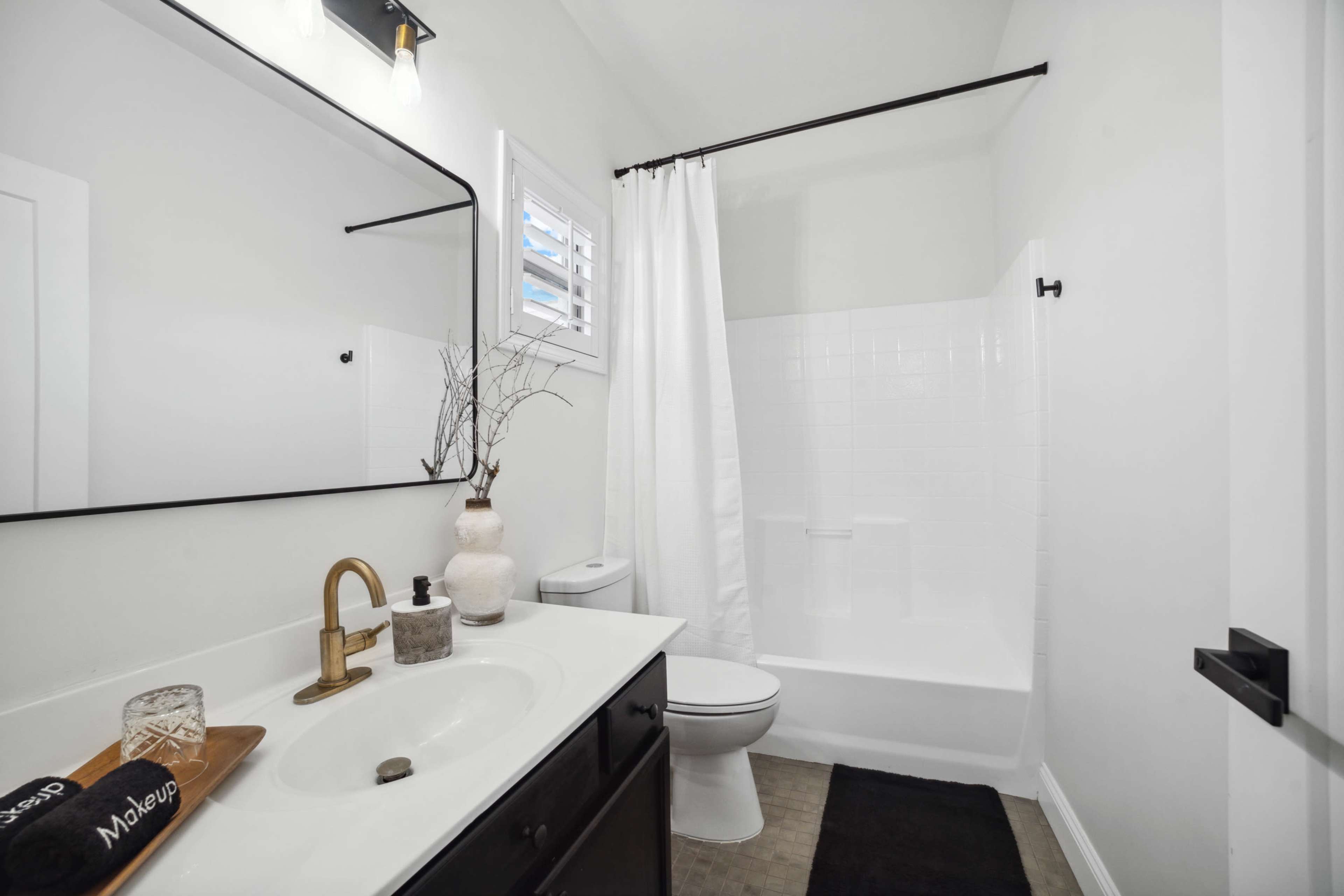 The bathroom features a white wall and tiled shower, a dark vanity with a sink, and minimal decorative elements.