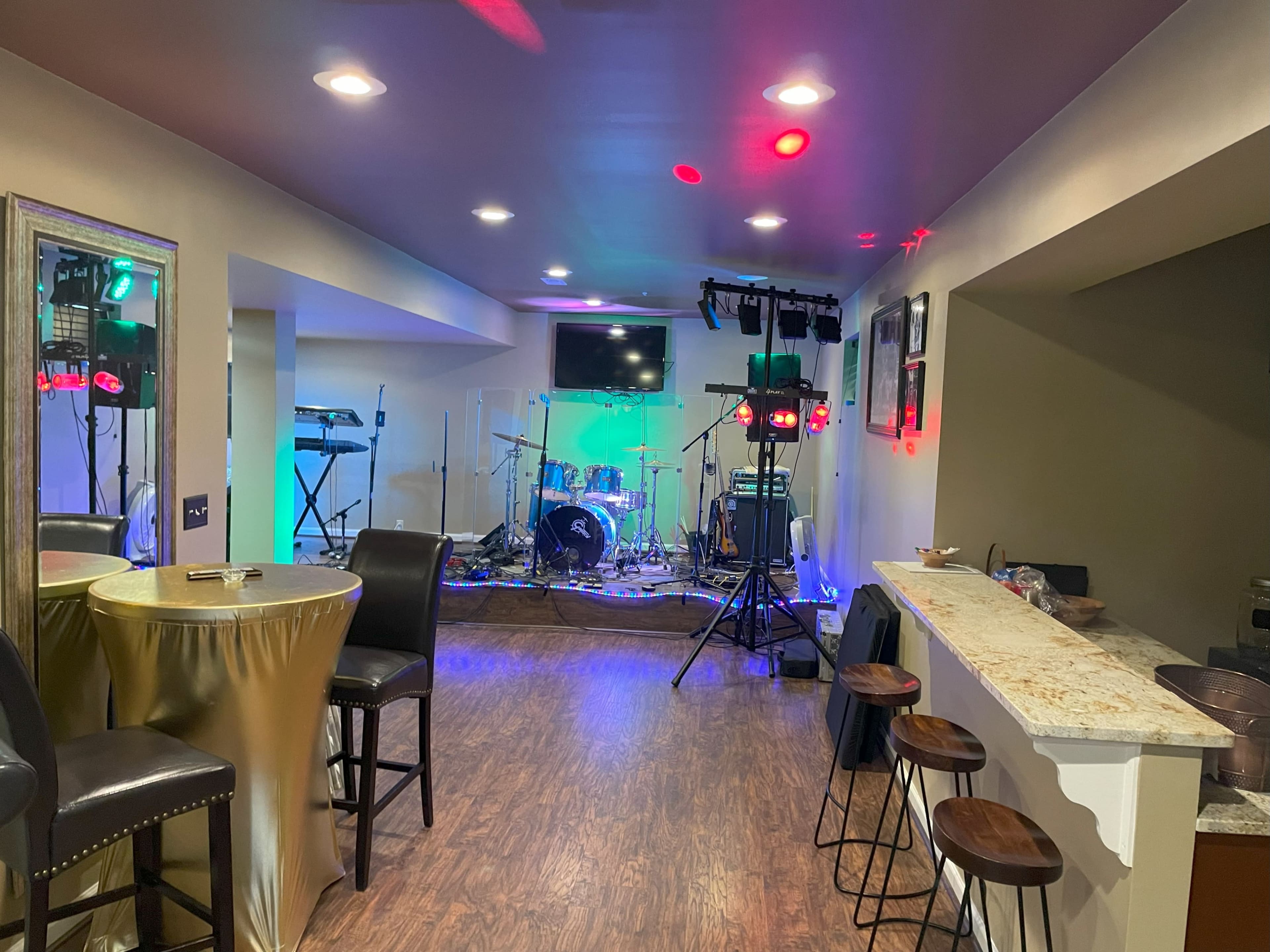 A small music venue featuring a stage set up with instruments, a bar area with stools, and tables.
