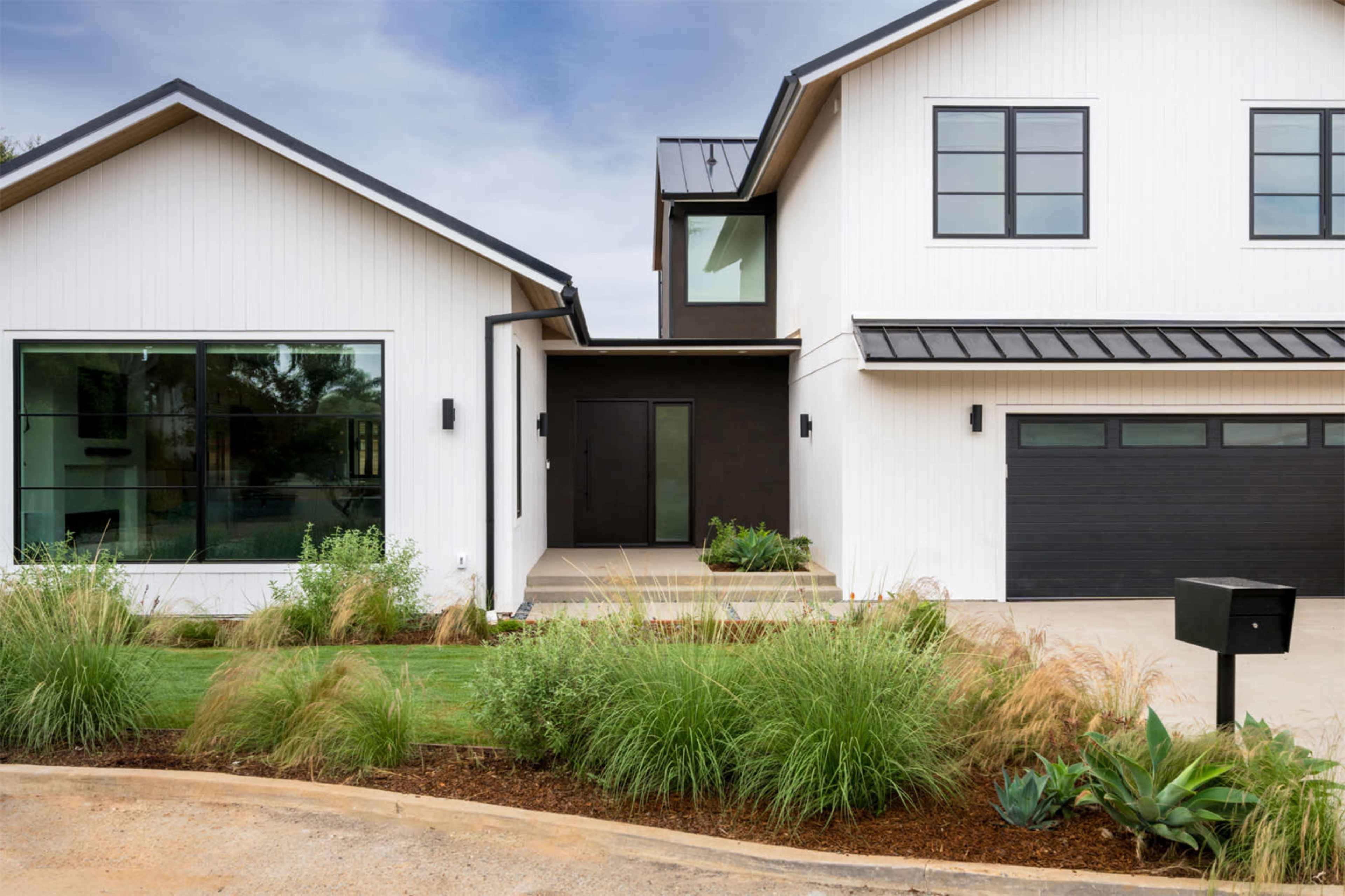 A modern two-story house features a combination of white siding and dark accents, with a landscaped entrance and a garage to the side.