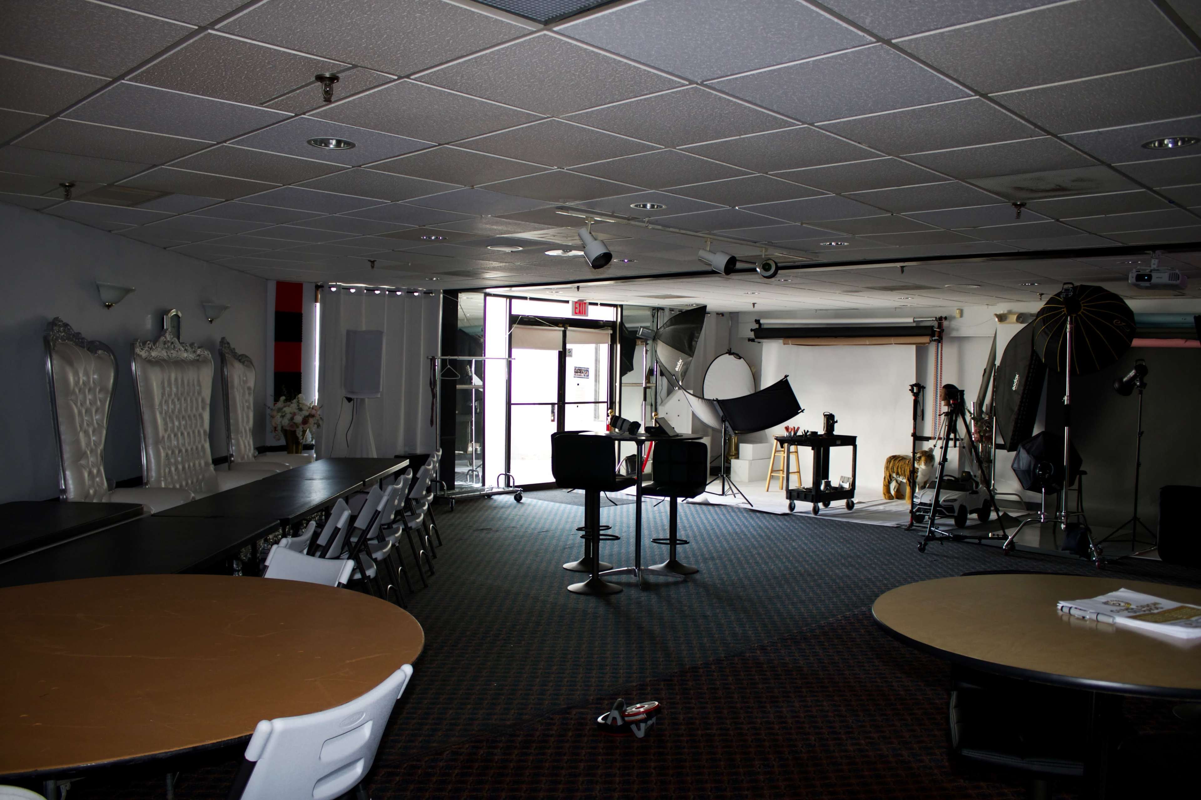 The image shows a photography studio with various equipment, chairs, and backdrops set up in a spacious, well-lit interior.