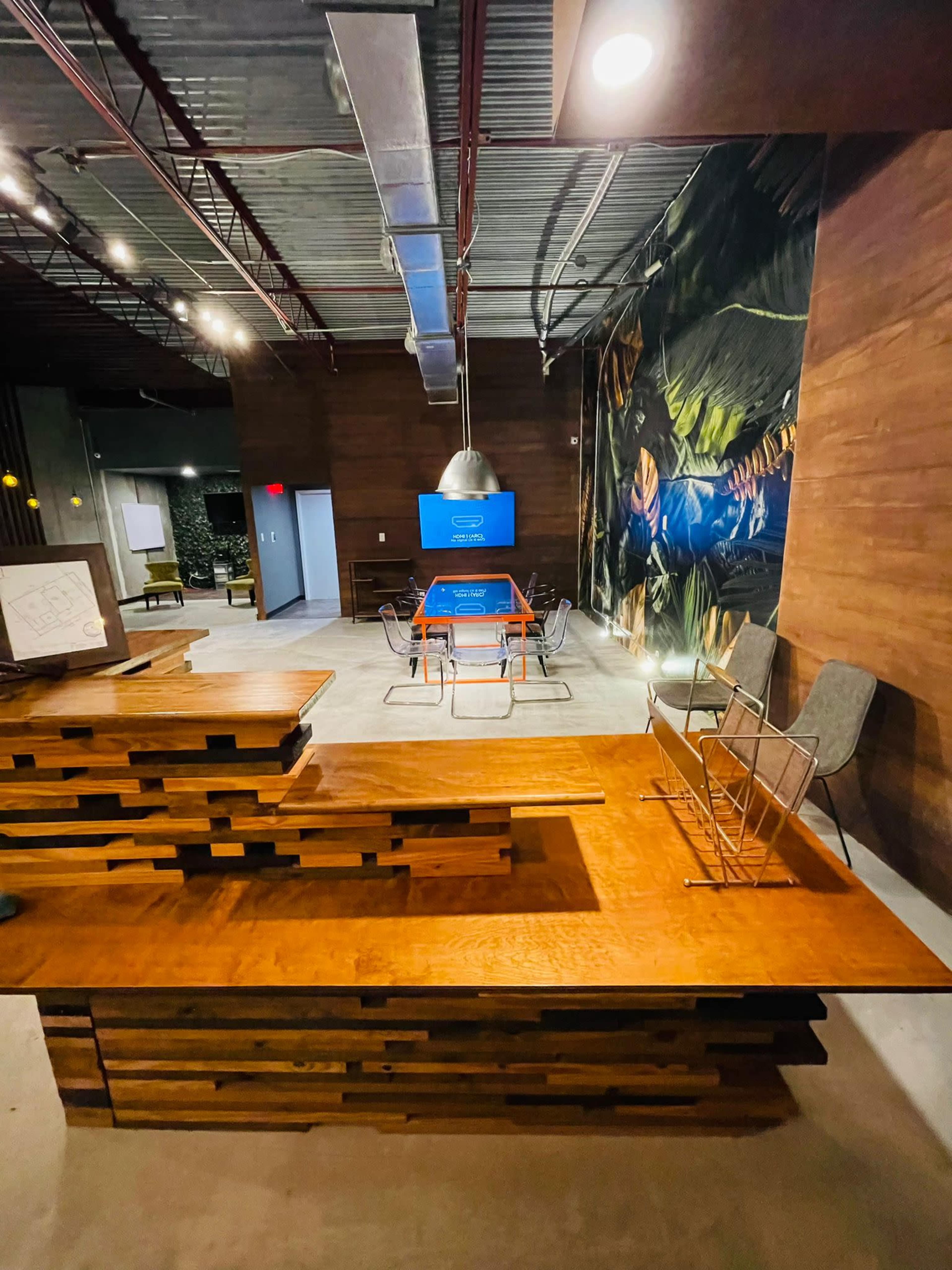 A modern office space featuring a wooden reception desk and a conference area with a large screen and several chairs.