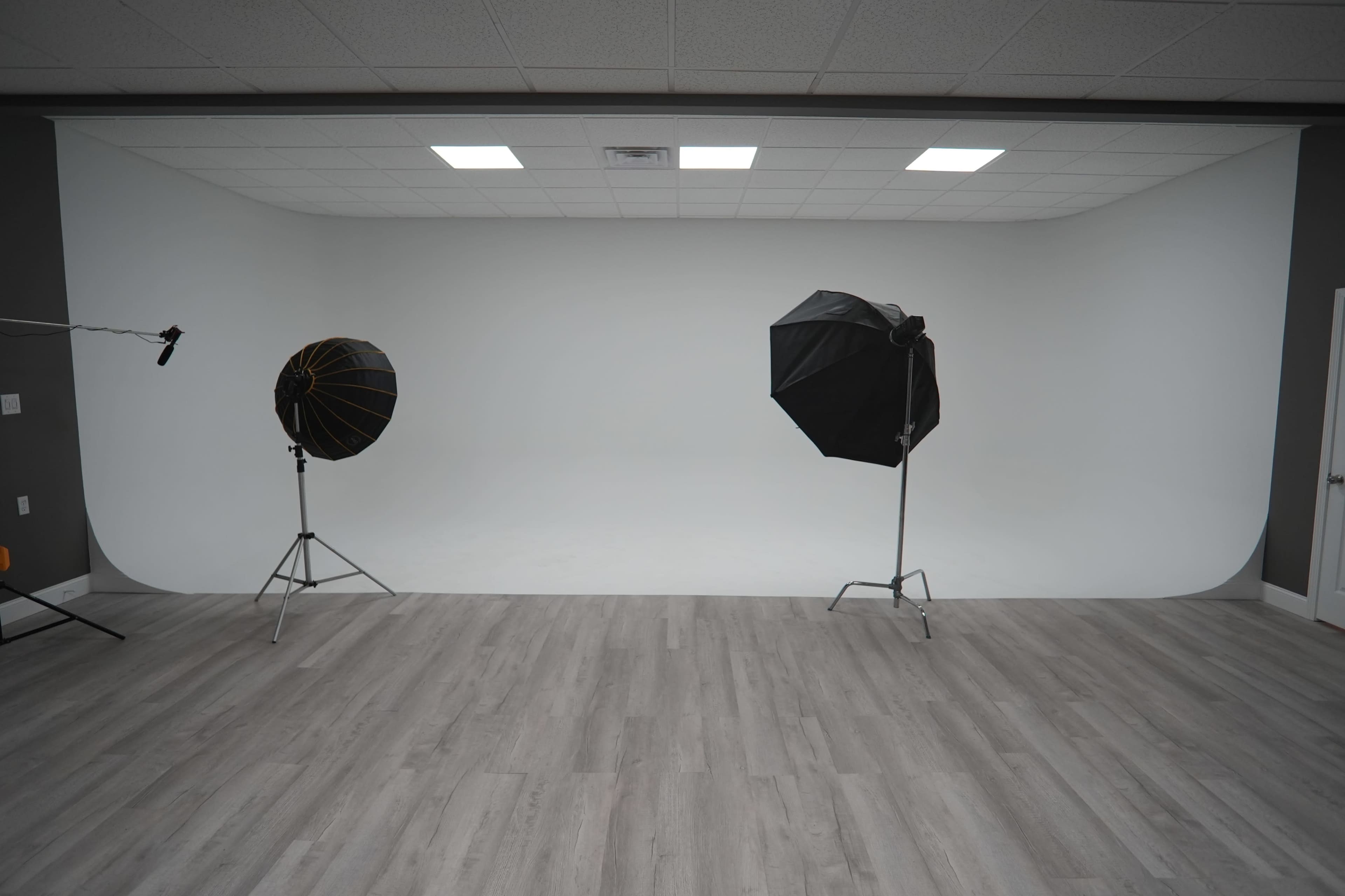 A photography studio features a white seamless backdrop flanked by two lighting umbrellas on stands.