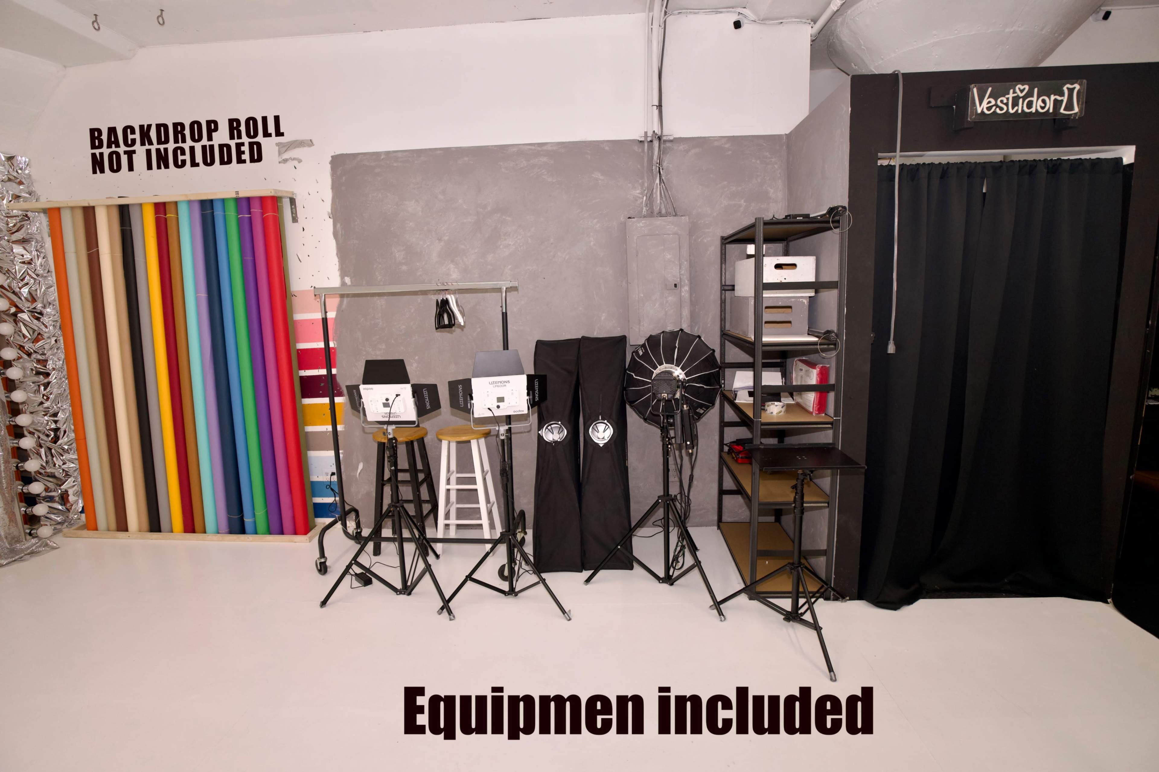 The image shows a photography studio setup featuring backdrop rolls, lighting equipment, and storage shelves against a textured wall.