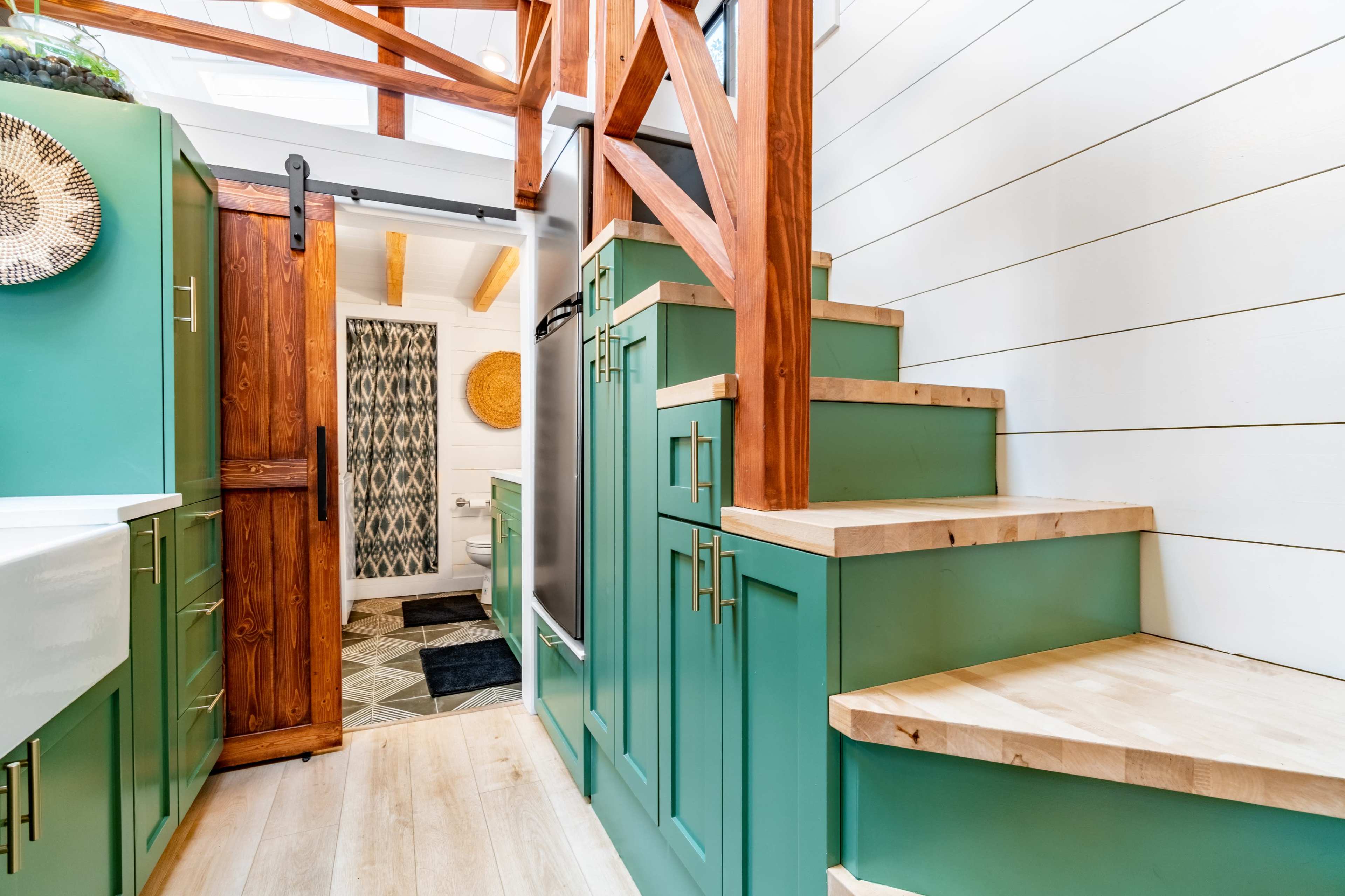 A compact kitchen and stairway with green cabinetry, a wooden door, and a light-colored floor.