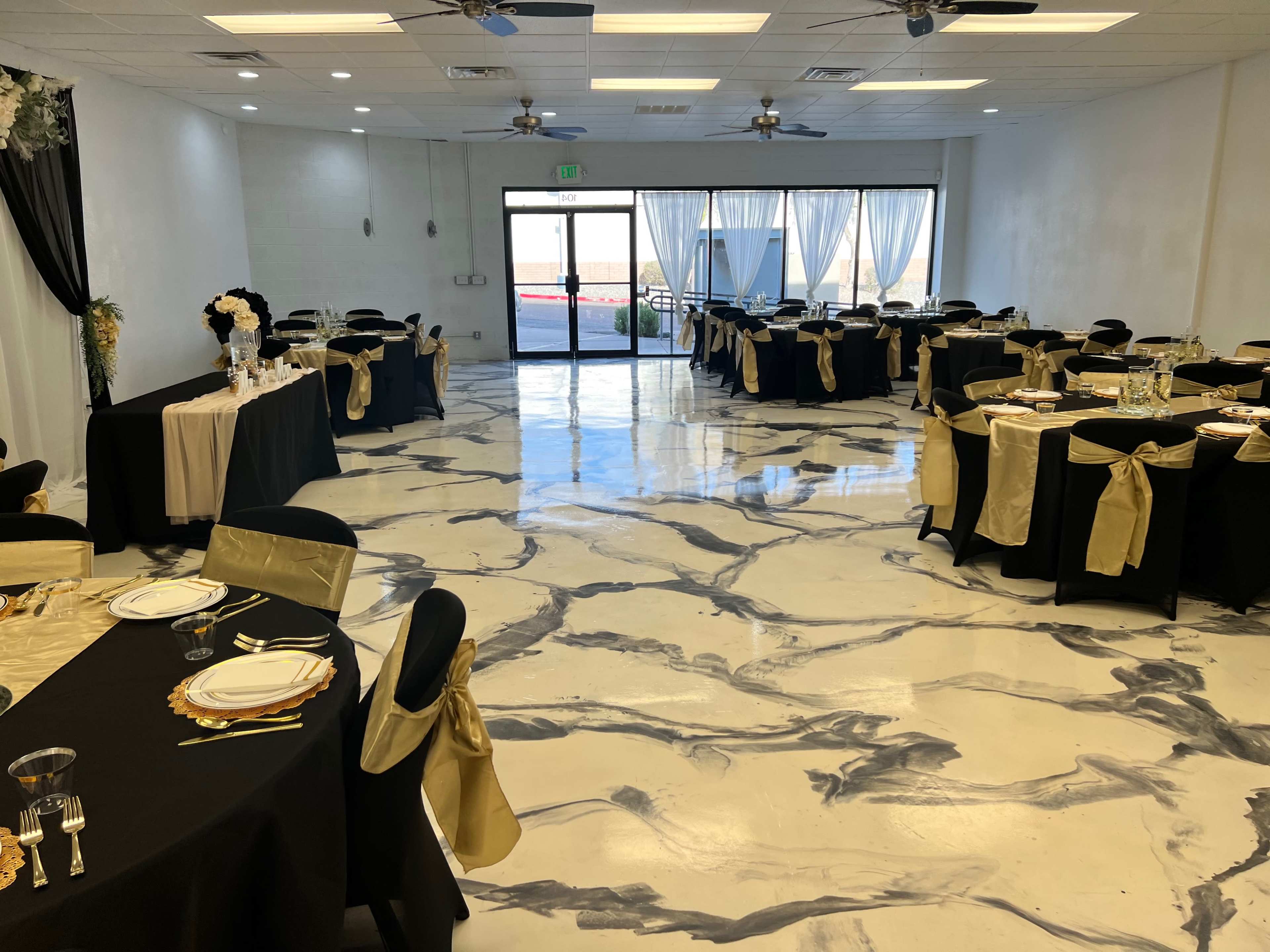 A banquet hall with tables set for an event, featuring black tablecloths, gold accents, and a polished marble-like floor.