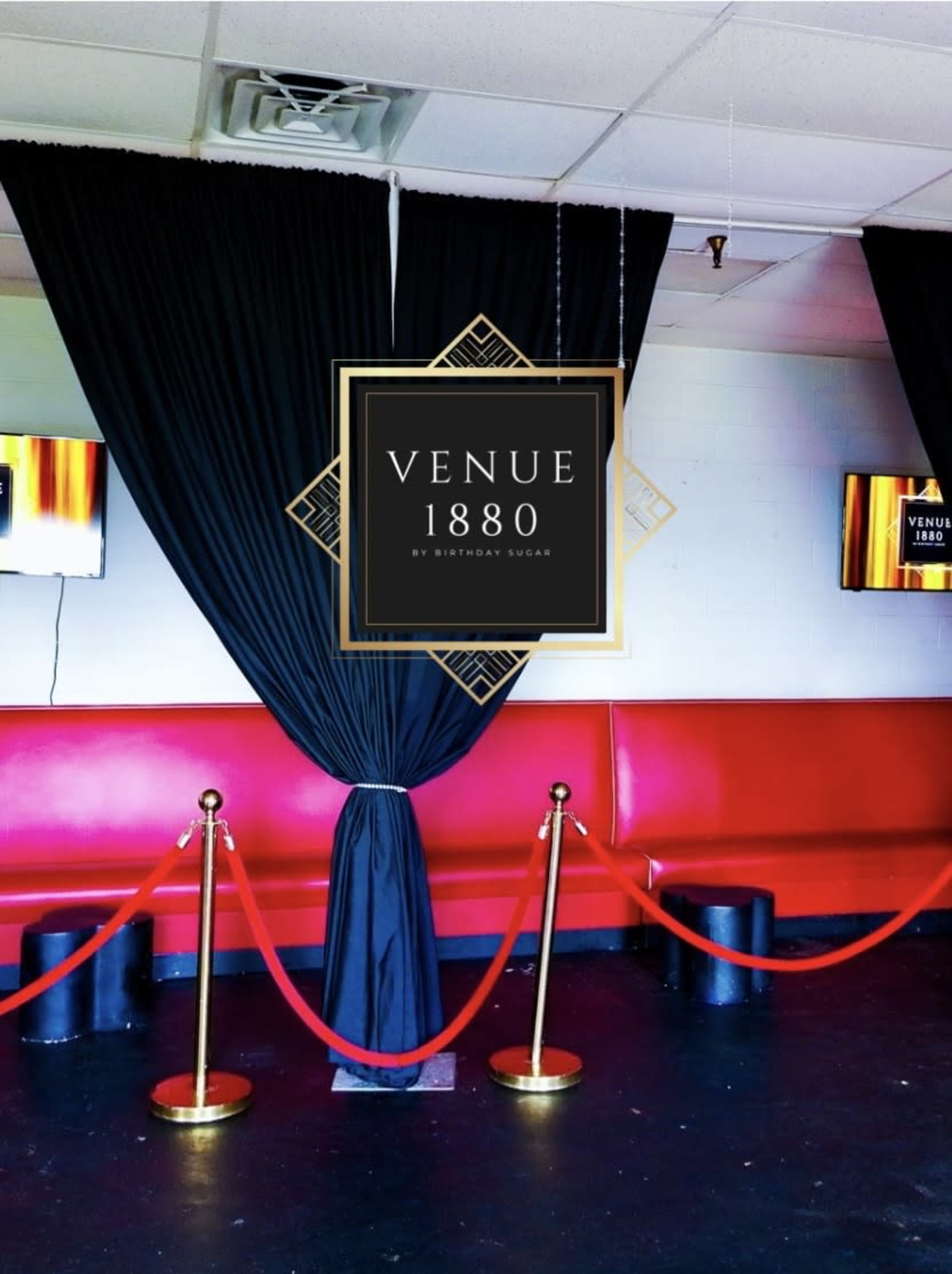 The image shows a corner of an event space with red benches, black drapes, and a gold stanchion rope.