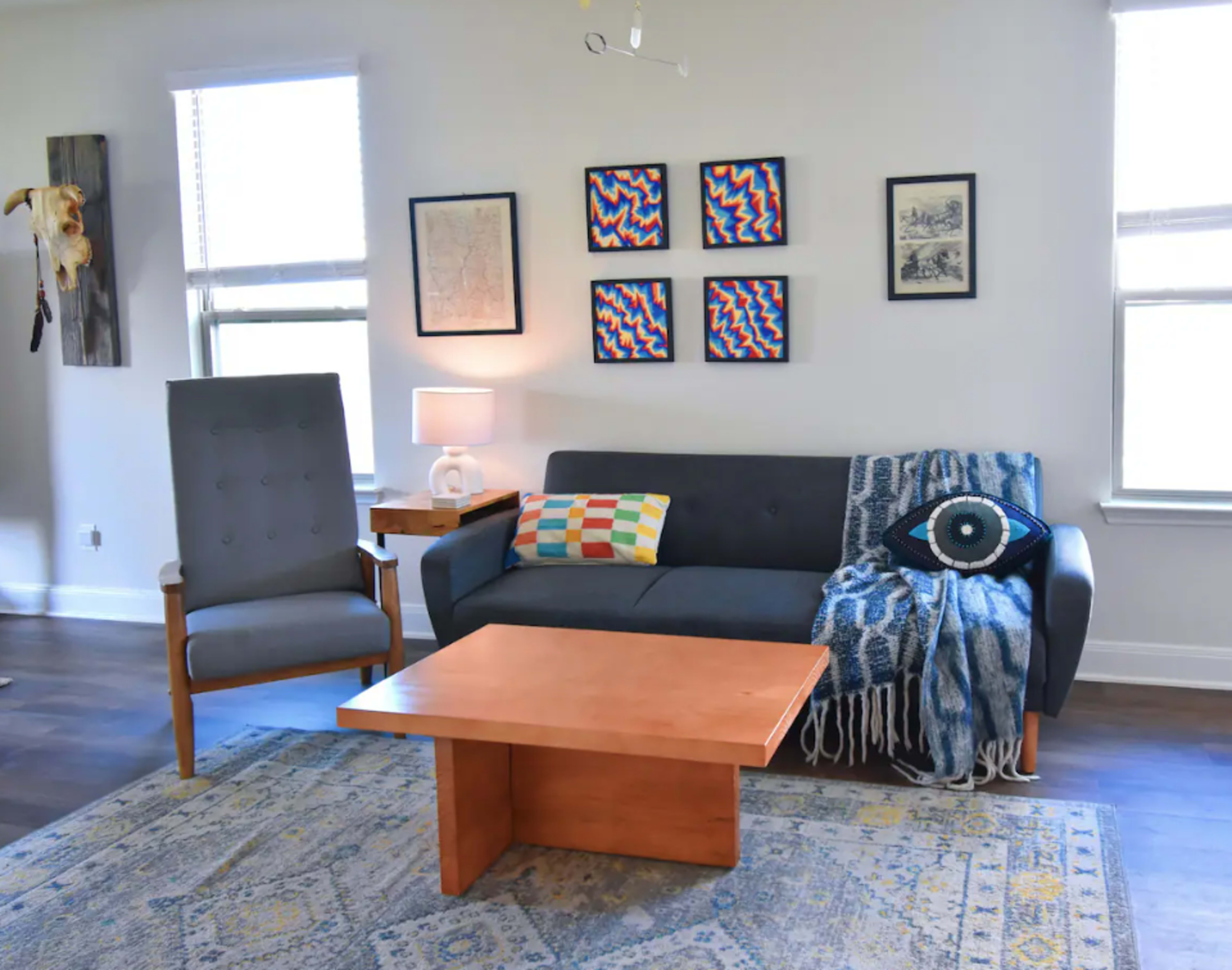 A living room with a gray sofa, a wooden coffee table, an armchair, and various framed artworks on the walls.