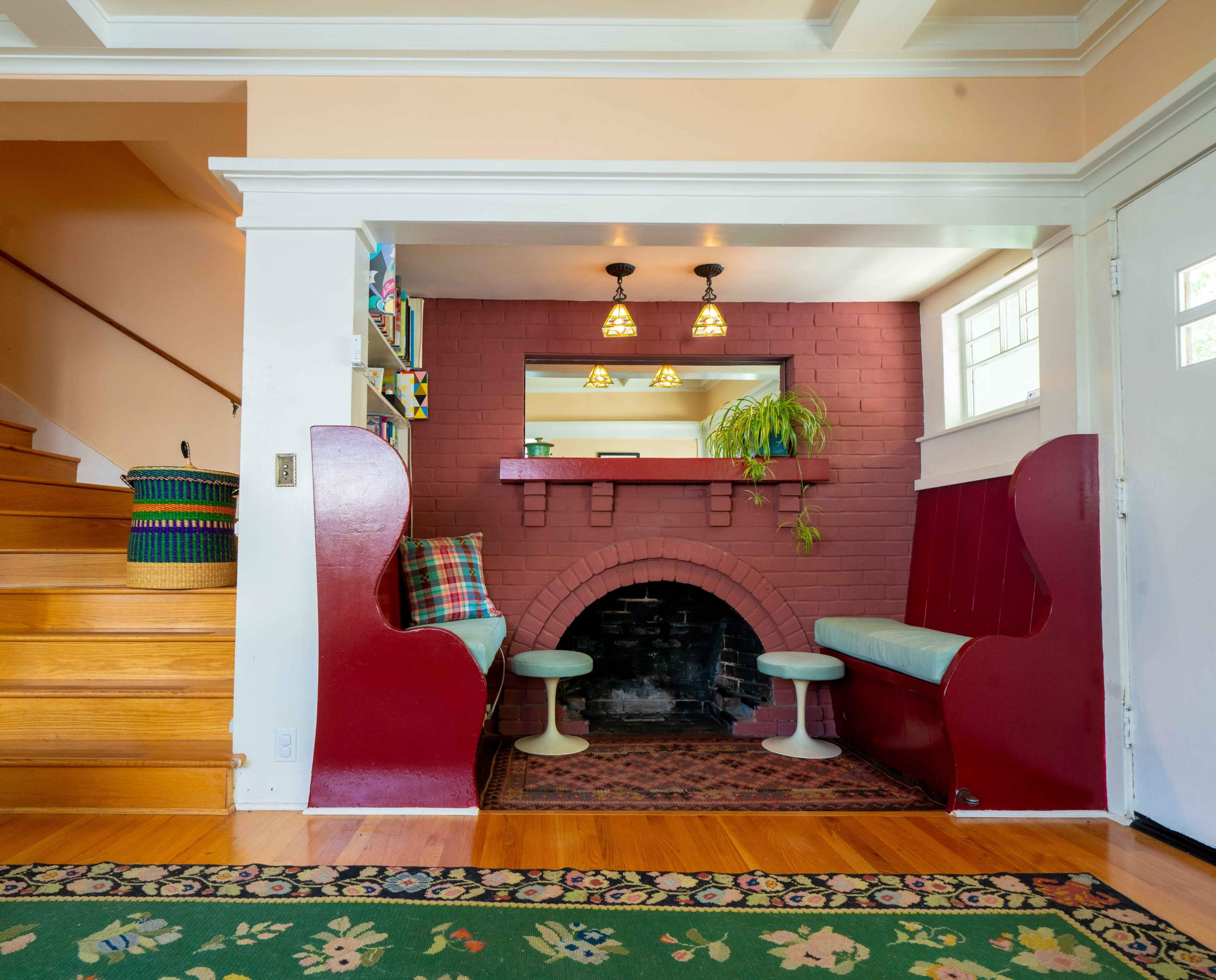 A cozy entryway featuring a red-brick fireplace with a mirror above, flanked by built-in benches and a wooden staircase leading to another level.
