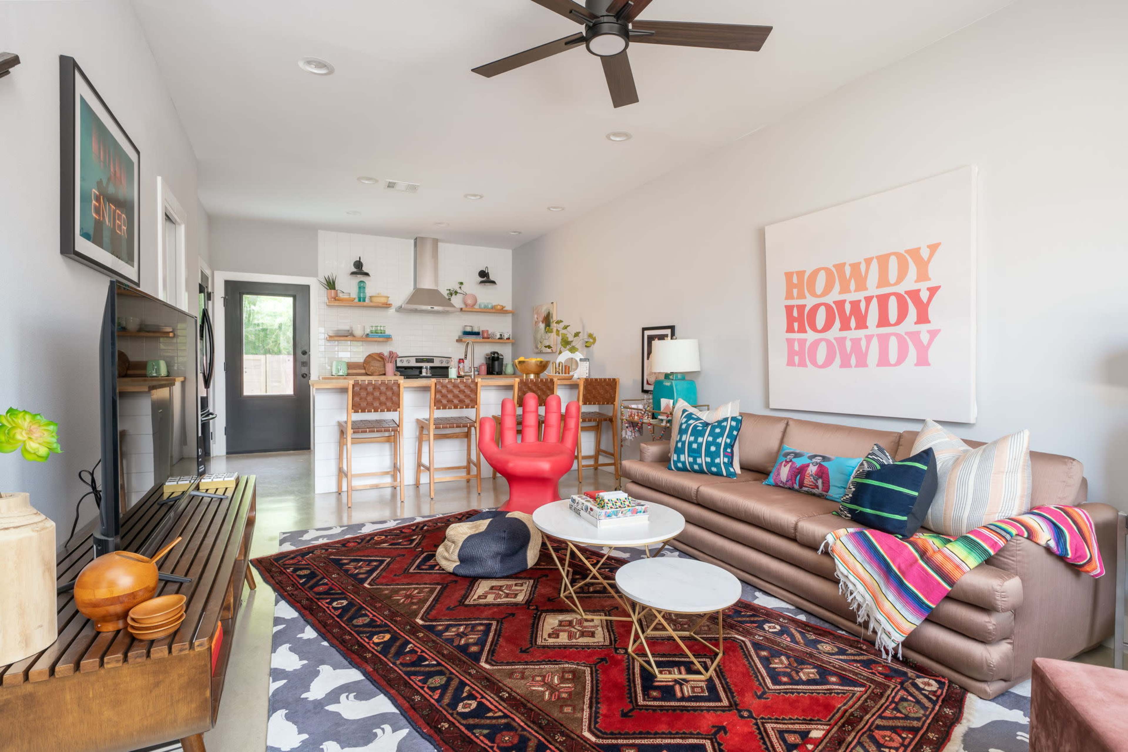 The living room features a brown sofa, a large red hand-shaped sculpture, and a dining area with bar stools in the background.