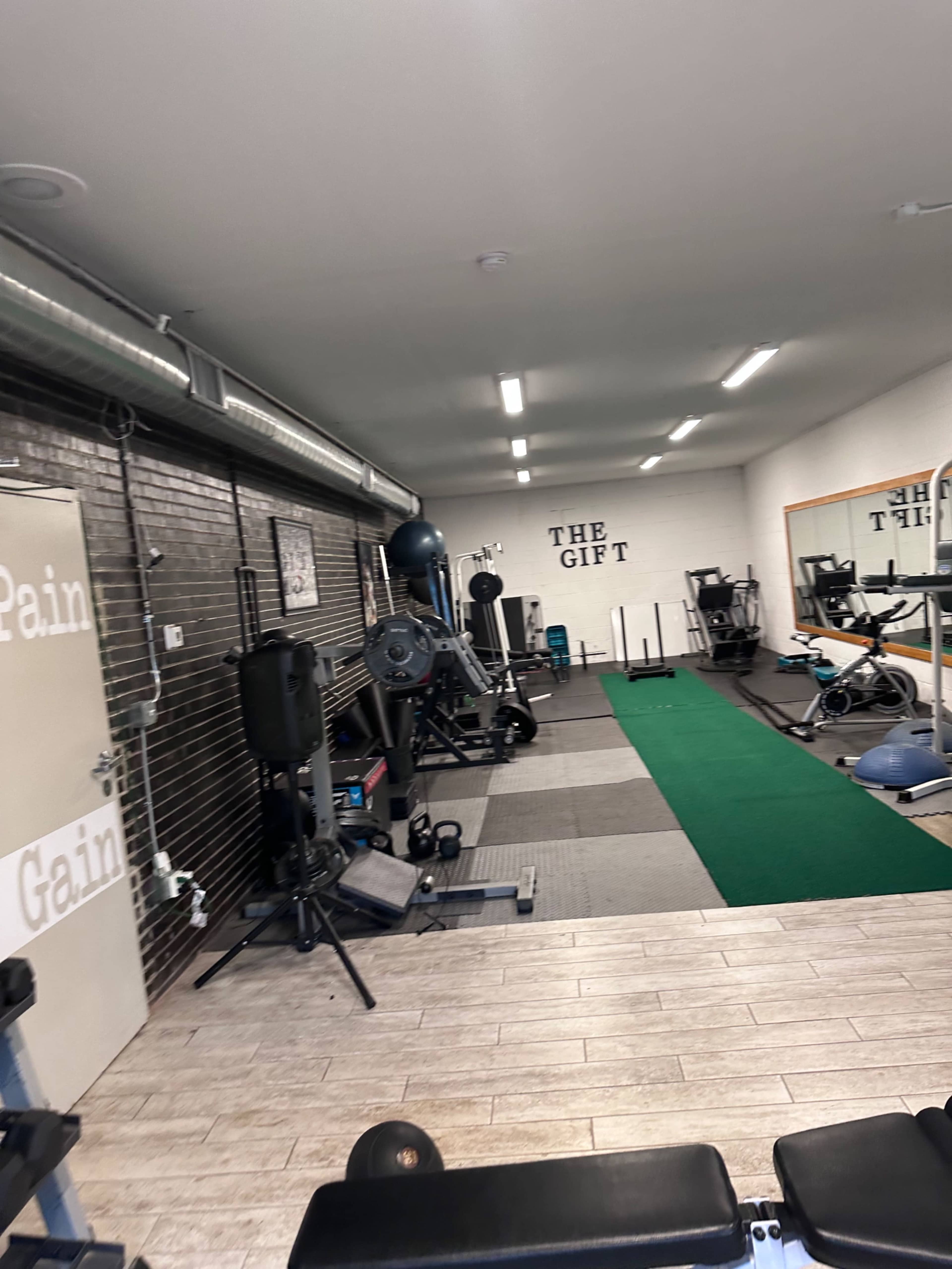 A gym interior featuring various exercise equipment, a green workout mat, and motivational signs on the walls.
