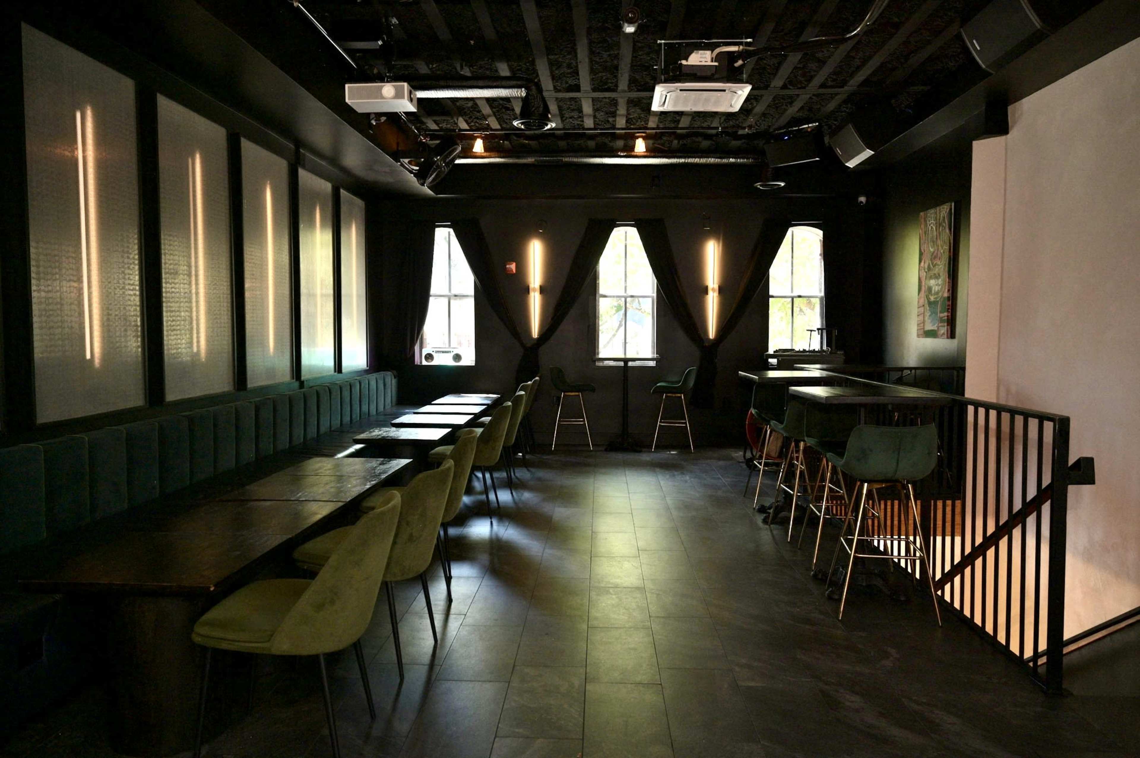 The image shows a dimly lit interior of a modern restaurant or bar with a mix of seated dining areas and high-top tables.