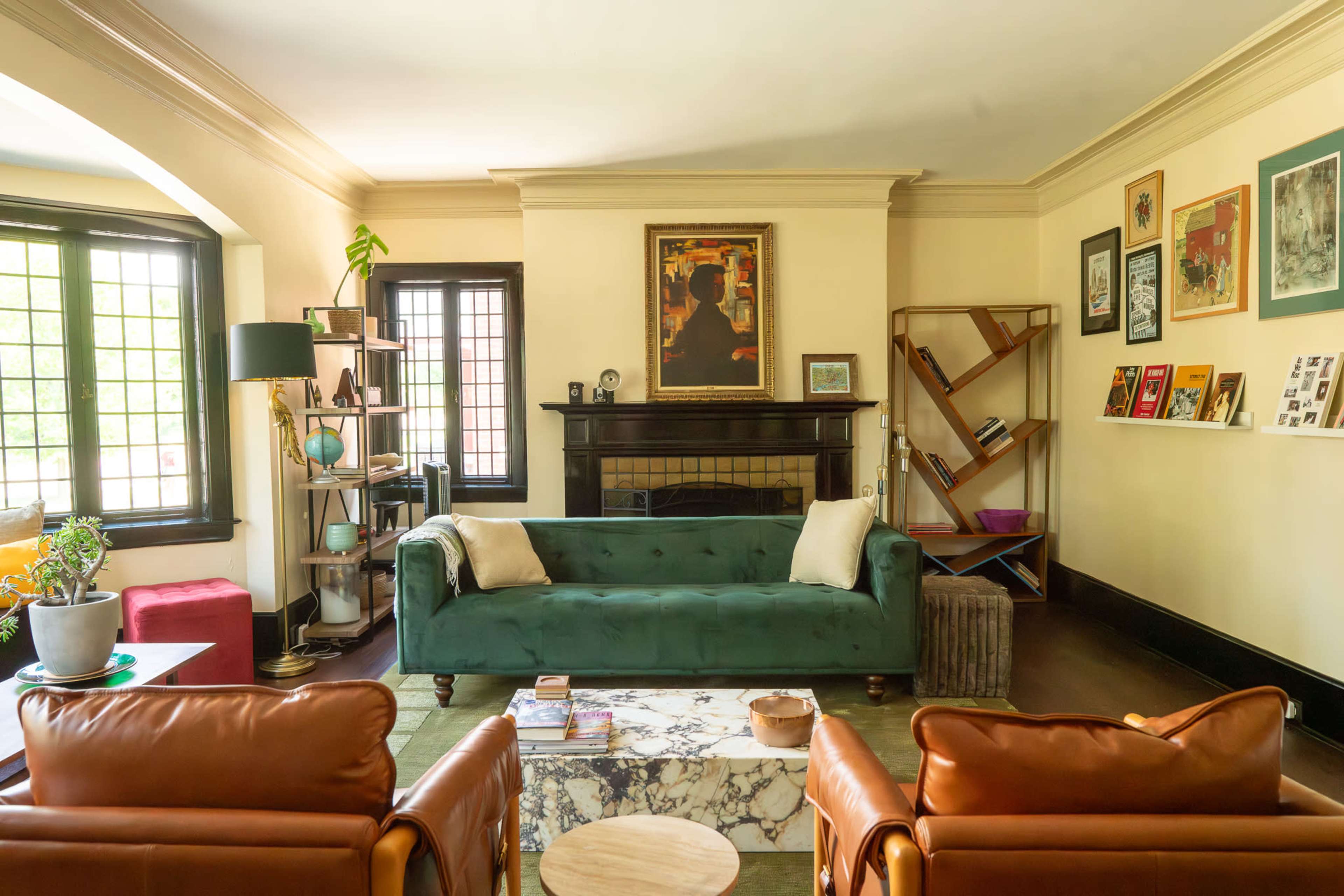The room features a green velvet sofa facing two brown leather chairs, with a marble coffee table and various artworks displayed on the walls.
