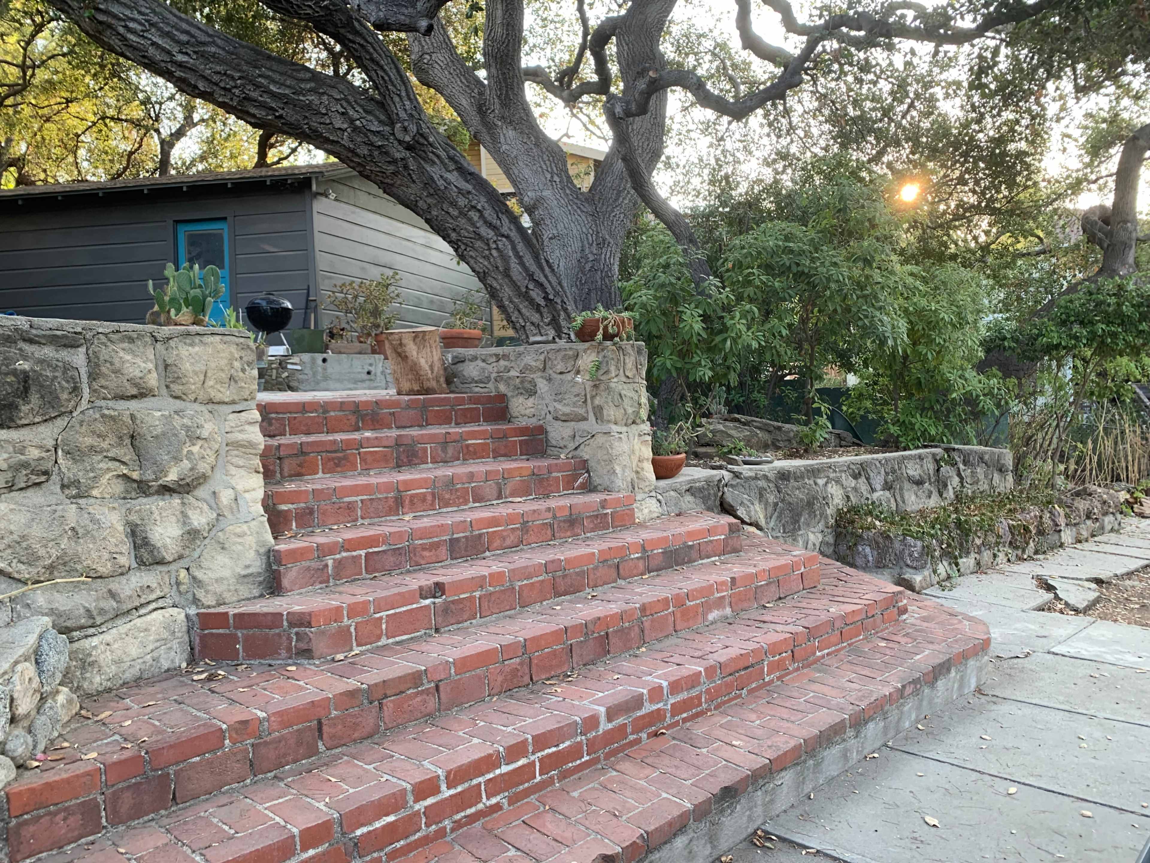 A series of brick steps leading up to a house surrounded by trees and plants.