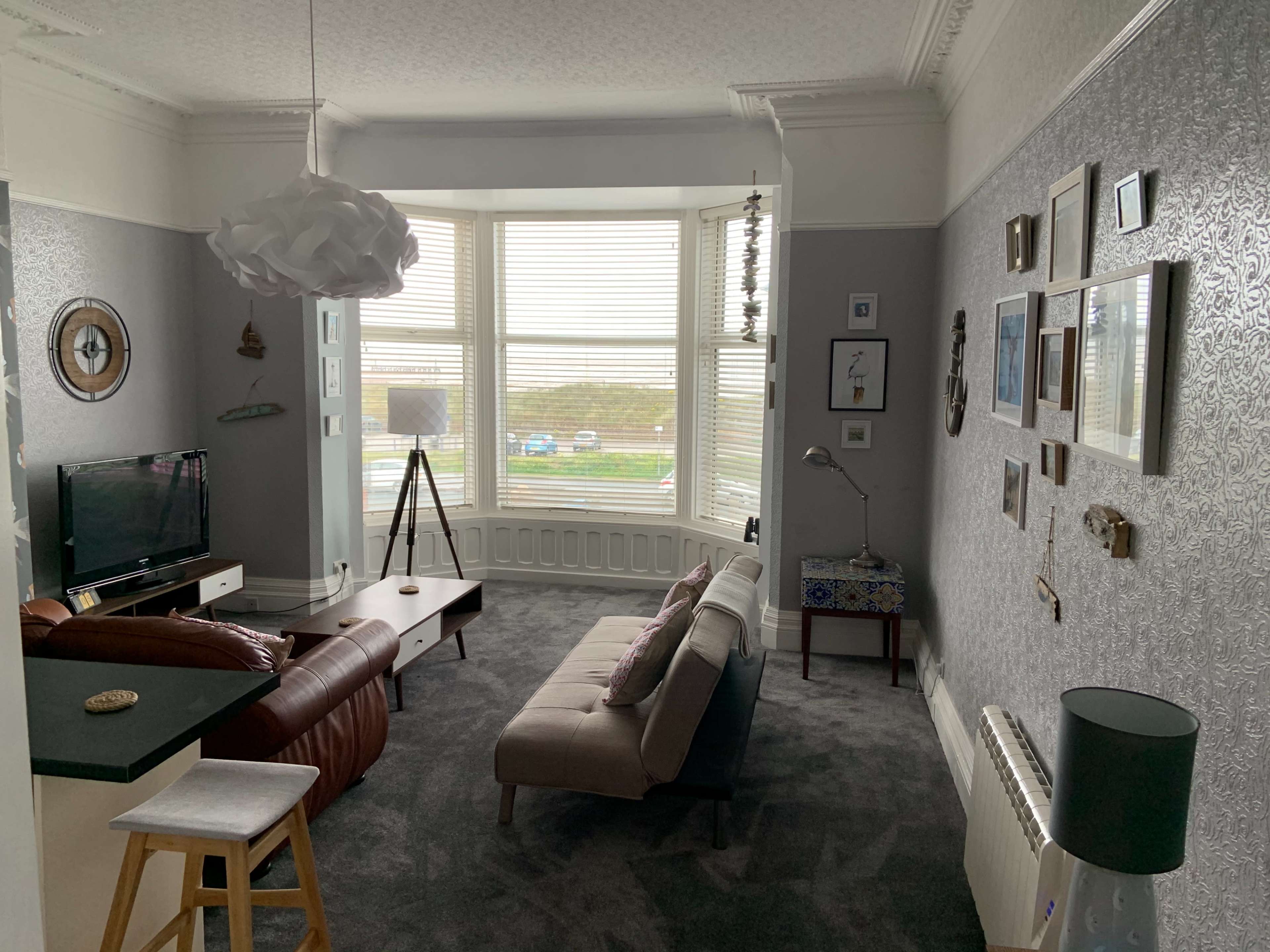 The living room features a bay window with striped blinds, a television, a sofa, a coffee table, and various artworks on the walls.