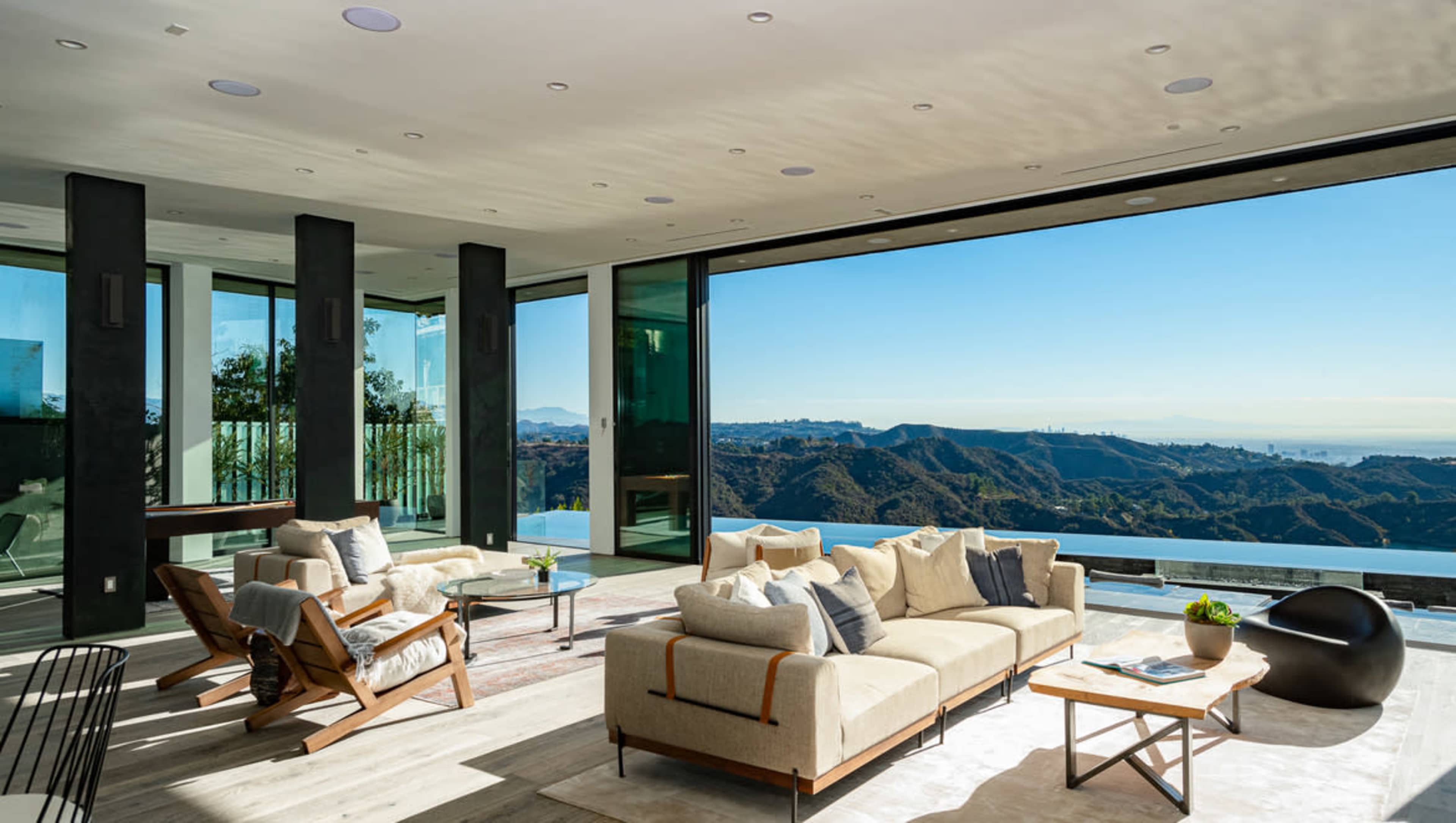 A modern living room features large glass windows that open to a view of rolling hills and clear blue skies.