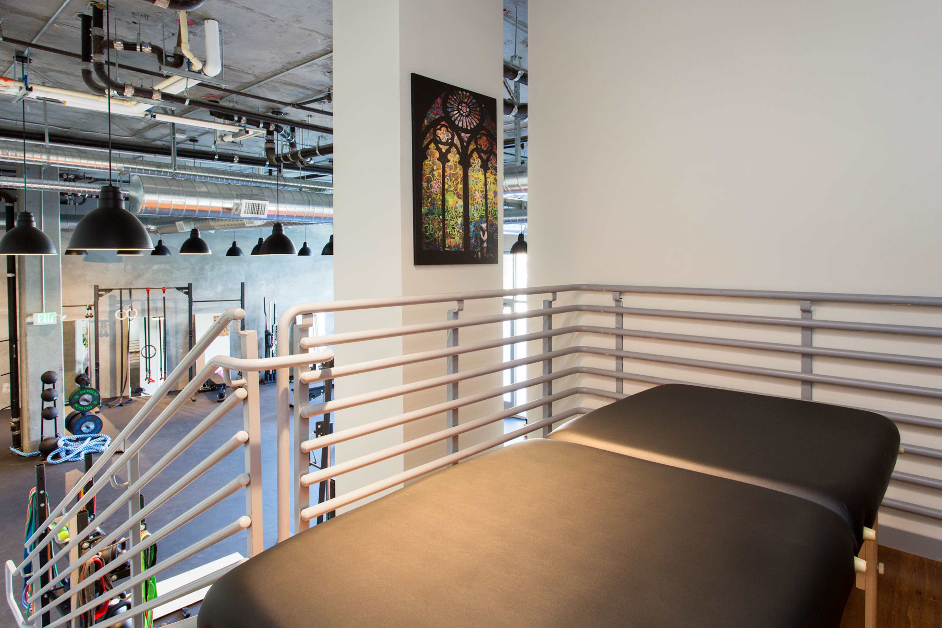 A training facility with exercise equipment visible in the background and a massage table on a balcony overlooking the space.
