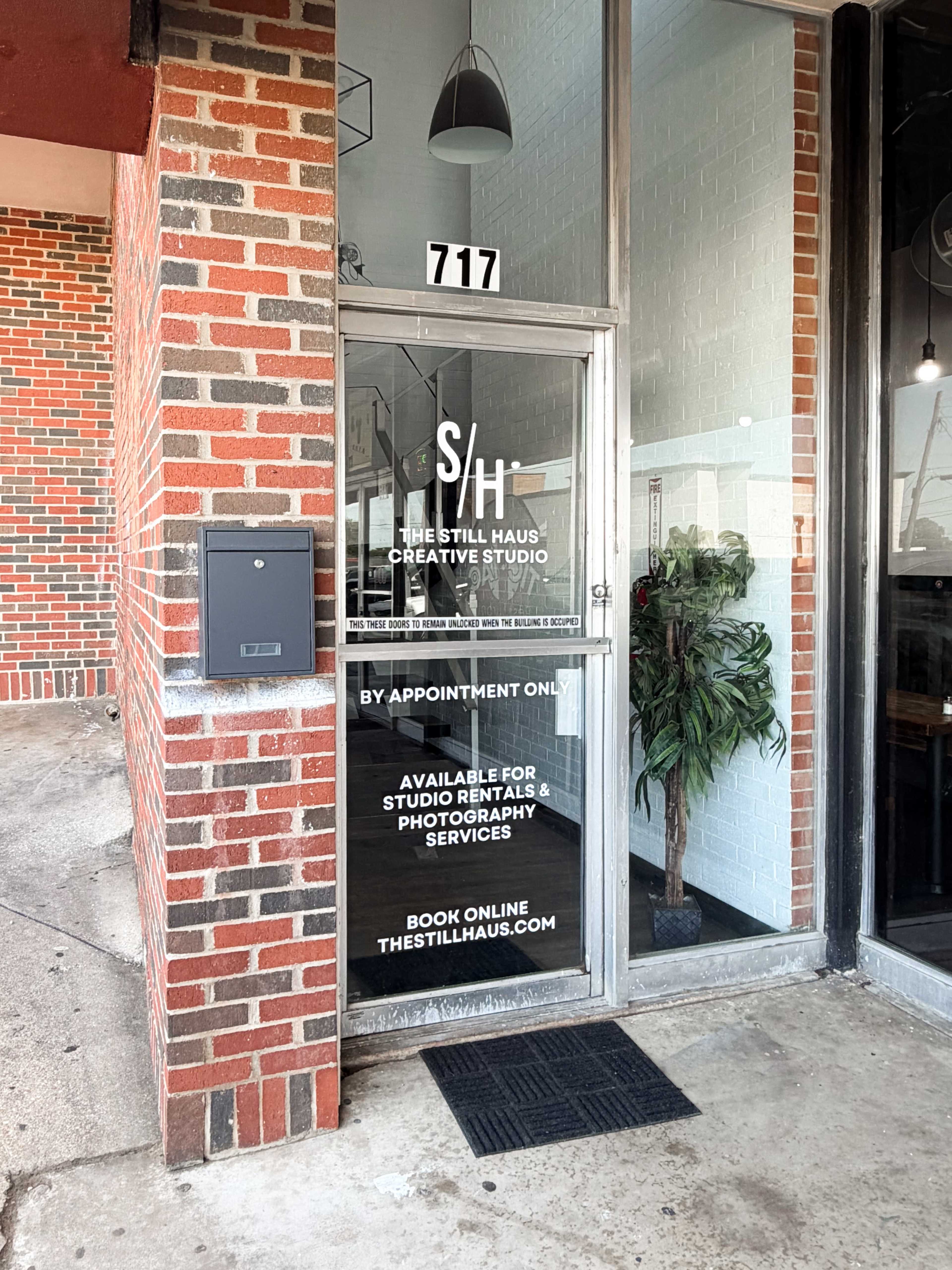 The image shows the entrance of The Still Haus Creative Studio, featuring a glass door with a sign indicating it is available for studio rental and photography services by appointment only.