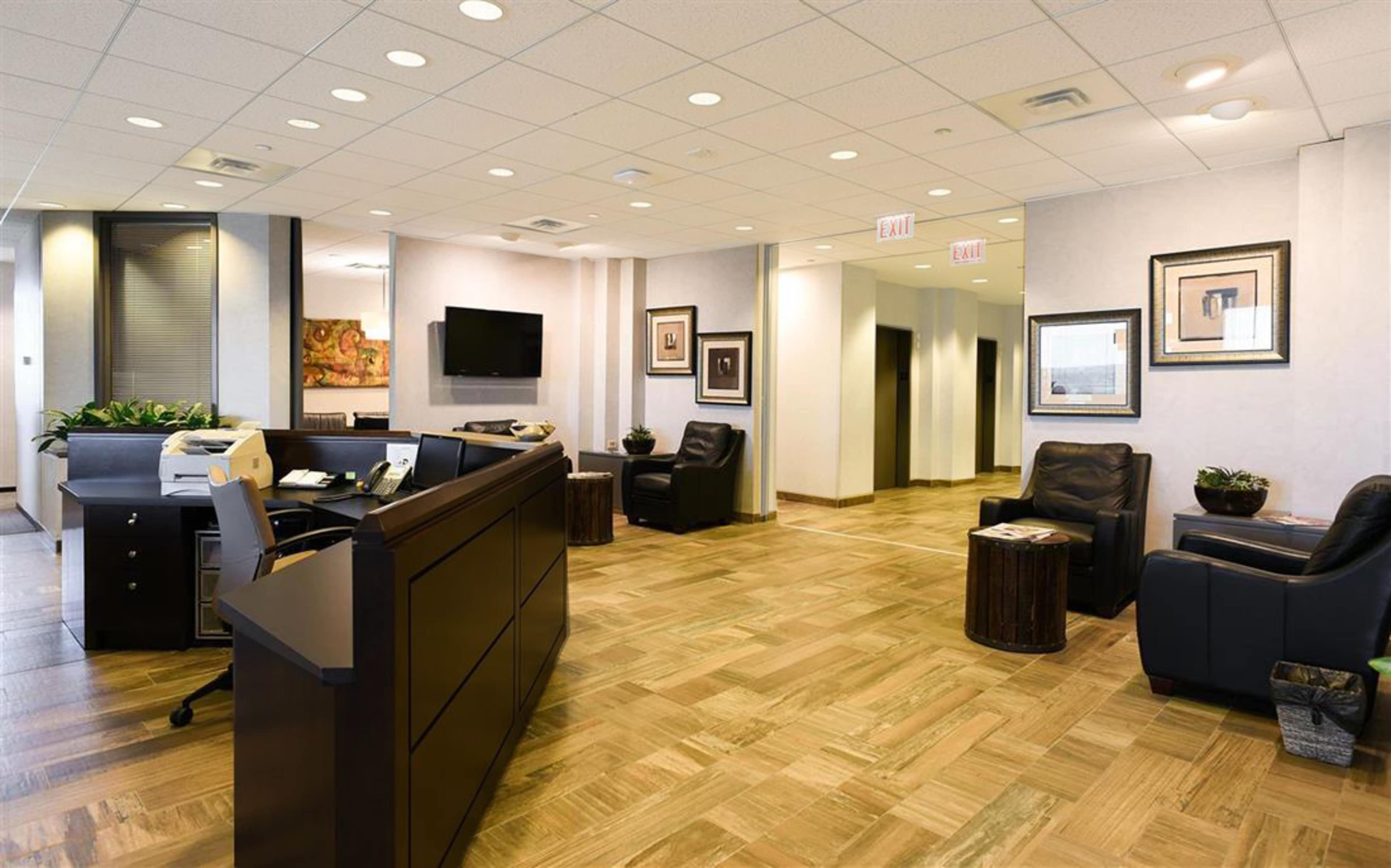 A modern office reception area features wooden flooring, dark furniture, and a seating area with leather chairs.
