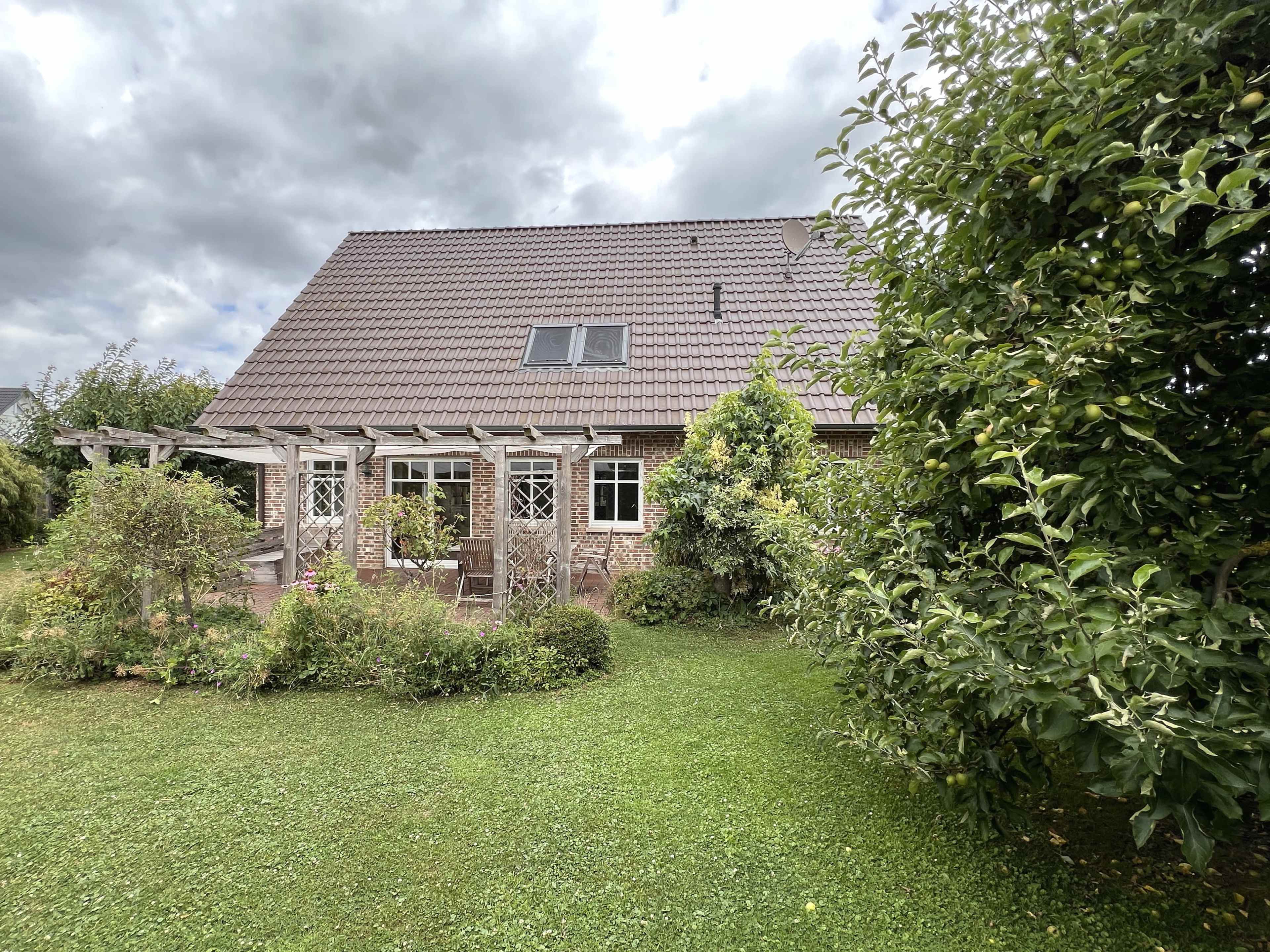 A two-story house with a brown tiled roof is surrounded by a green lawn and several trees.