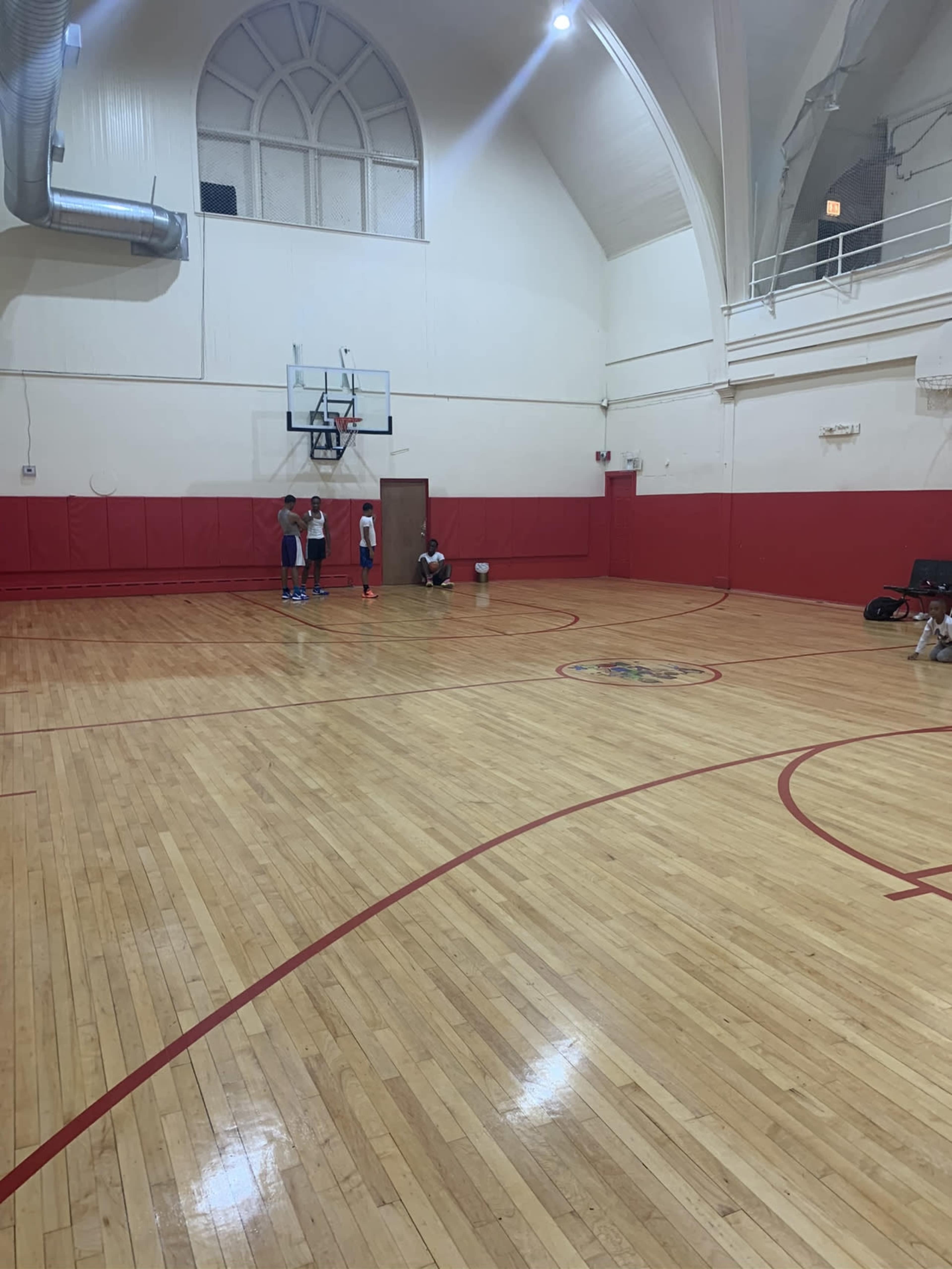 A group of four people is practicing basketball in a gymnasium with wooden floors and red walls.