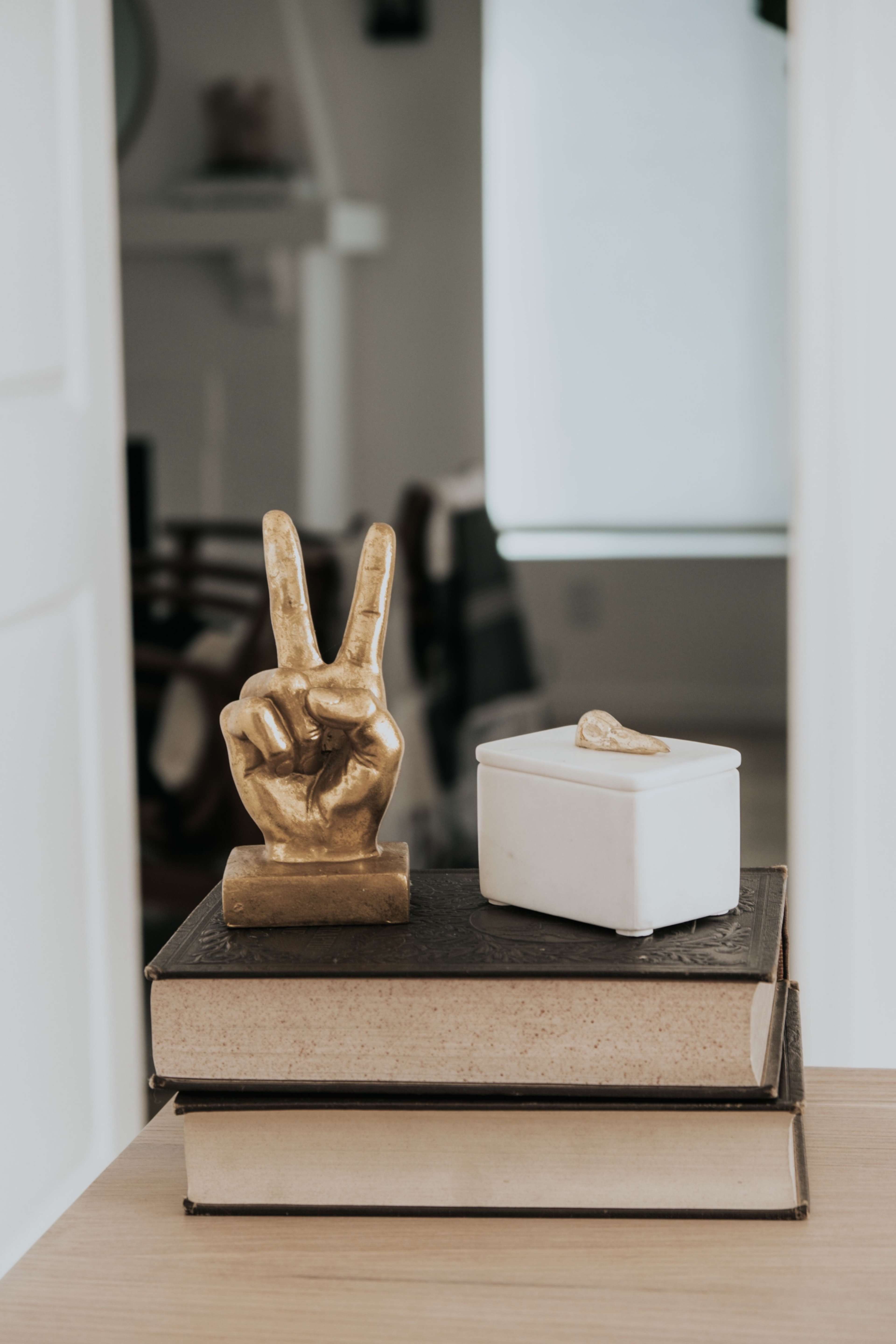 A gold hand figurine making a peace sign rests on top of stacked books next to a small white container.