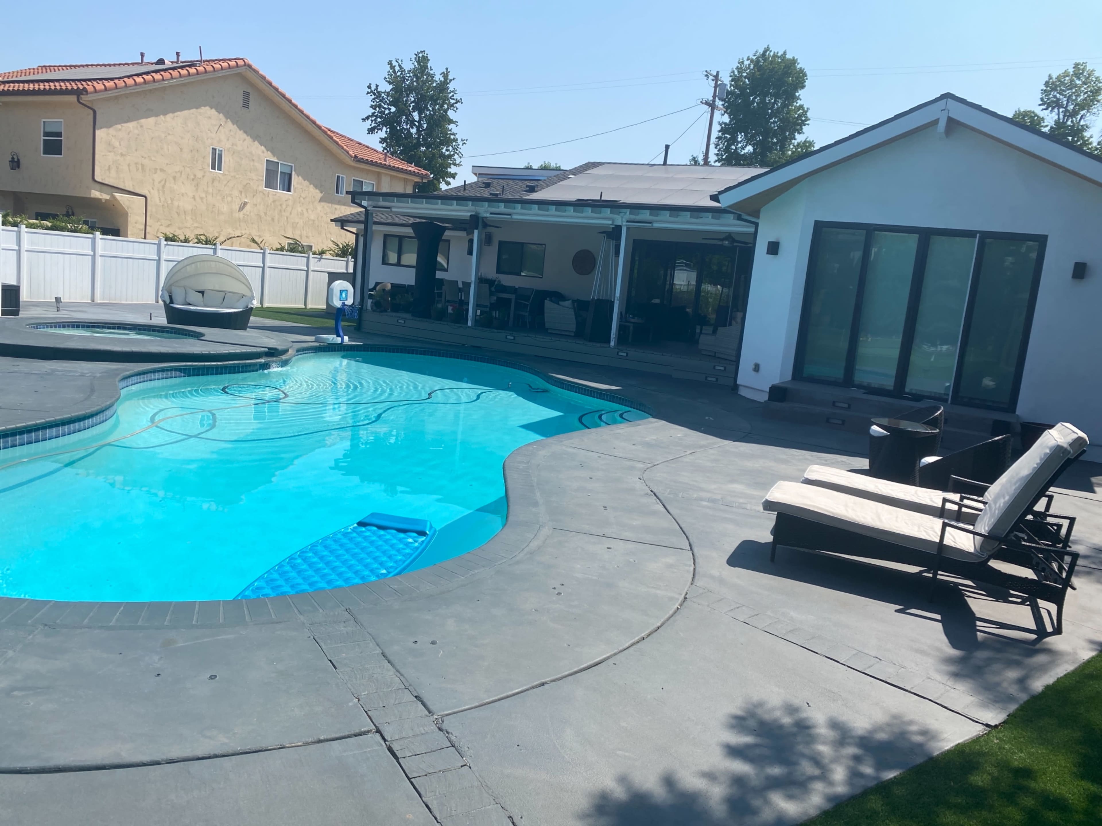 A landscaped backyard featuring a swimming pool, lounge chairs, and a modern house with large windows.